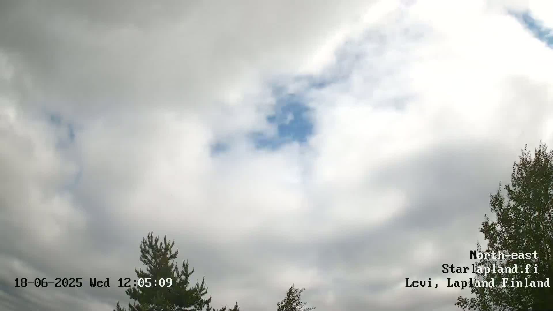 A mostly cloudy sky with patches of blue showing through, partially obscured by trees at the bottom of the frame.