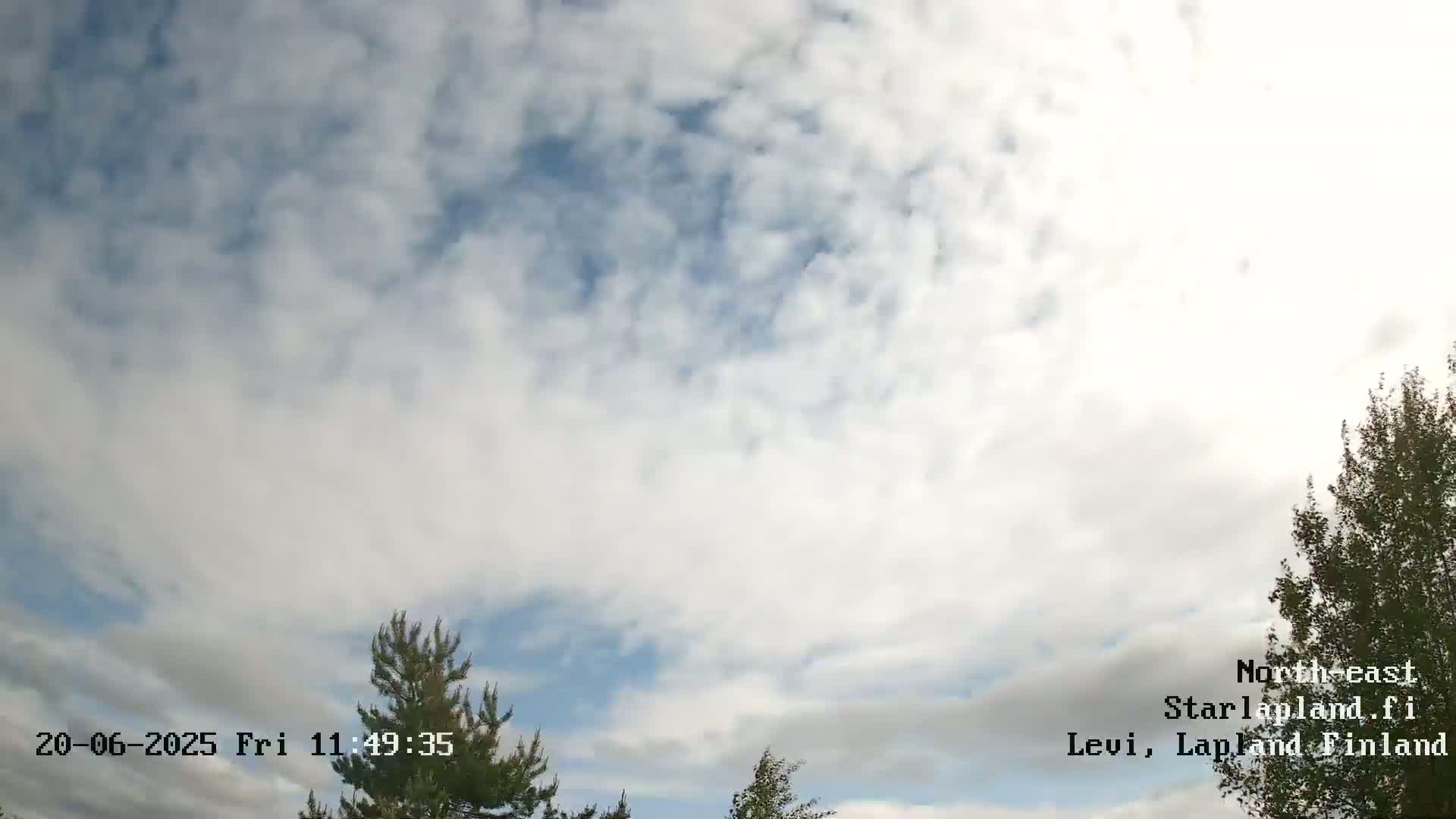 A partly cloudy sky is visible above some coniferous and deciduous trees.
