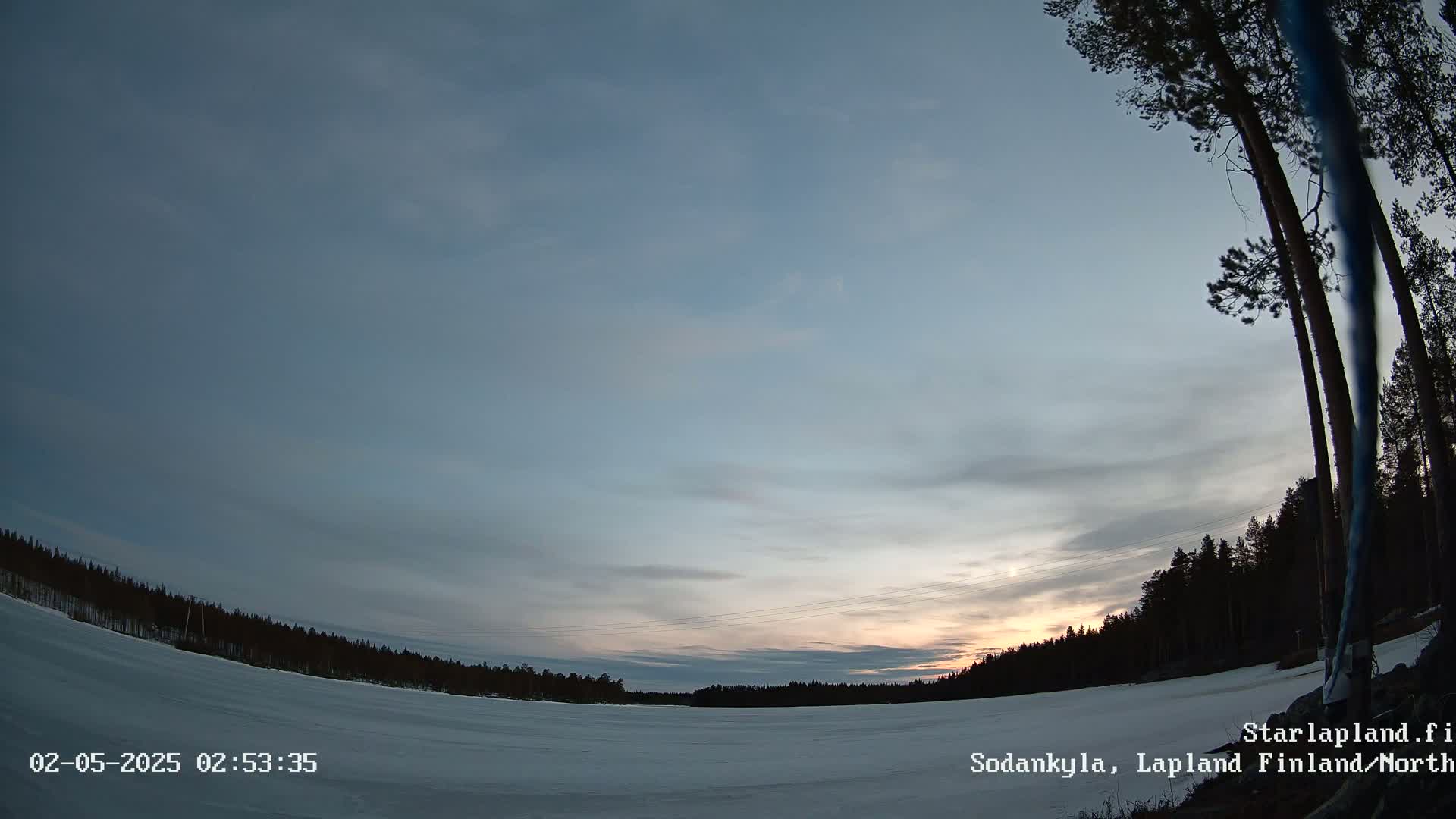 A snow-covered landscape at twilight under a mostly clear sky is shown, with a line of dark trees along the horizon.