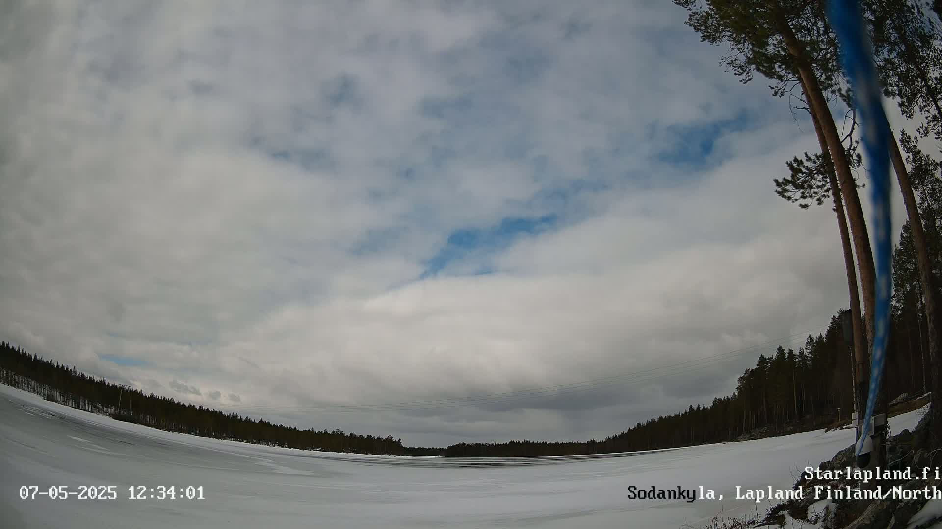 A mostly cloudy sky hovers over a frozen lake bordered by a dark coniferous forest.