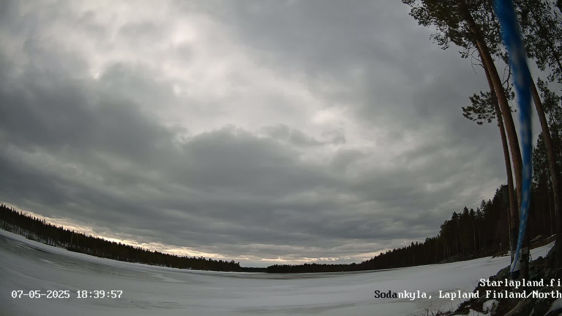 A snow-covered, frozen lake is visible beneath an overcast sky, bordered by a dark coniferous forest.