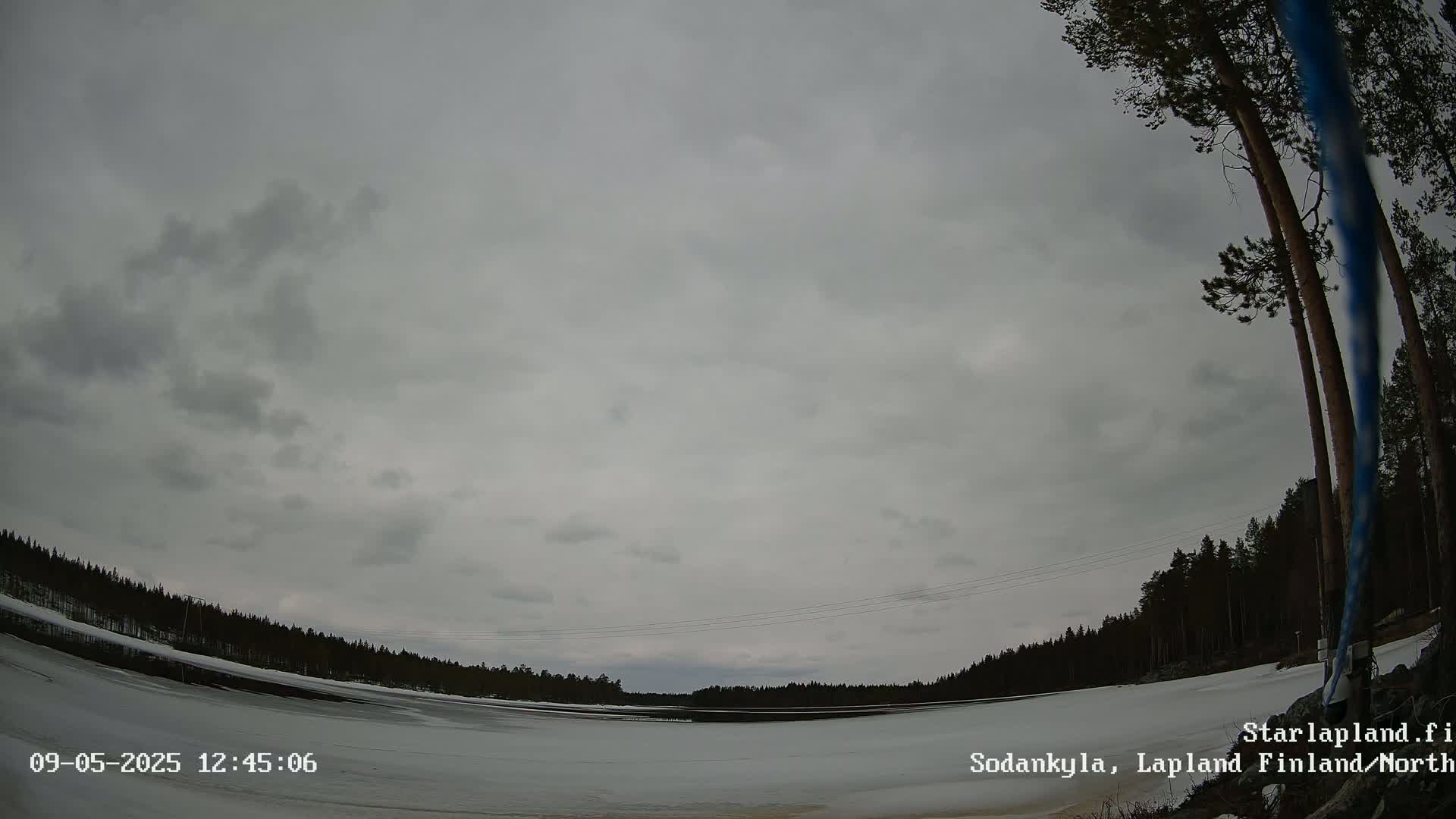 A mostly cloudy sky hangs over a snow-covered frozen lake and a dark pine forest under an overcast sky.