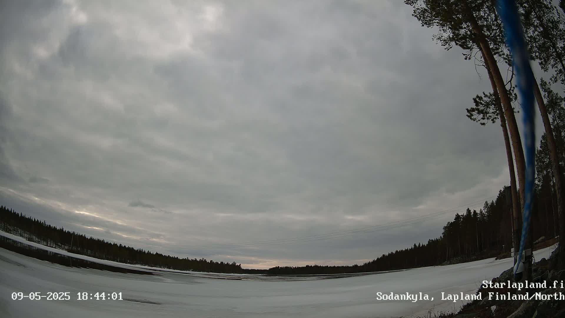 A snow-covered landscape with a dark, cloudy sky and a line of trees in the distance.