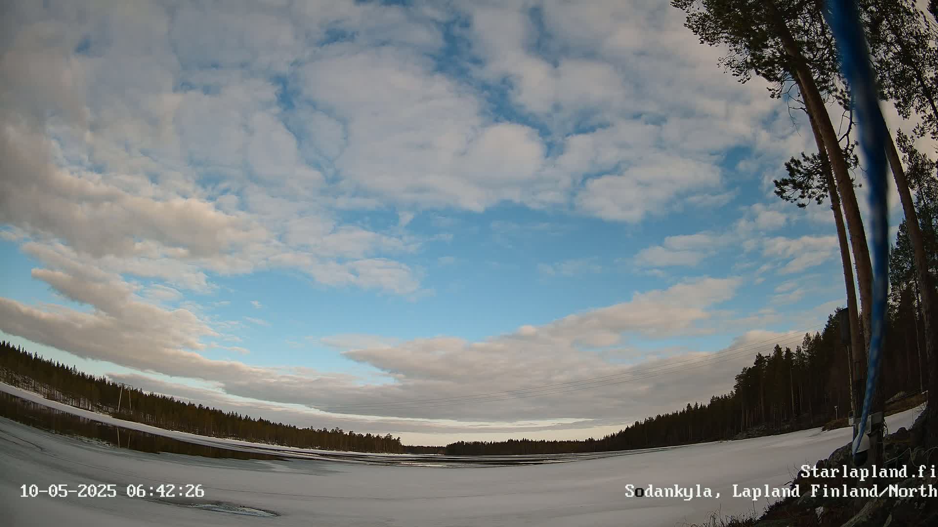 A partly cloudy sky over a snow-covered frozen lake with a dark forest line in the background.