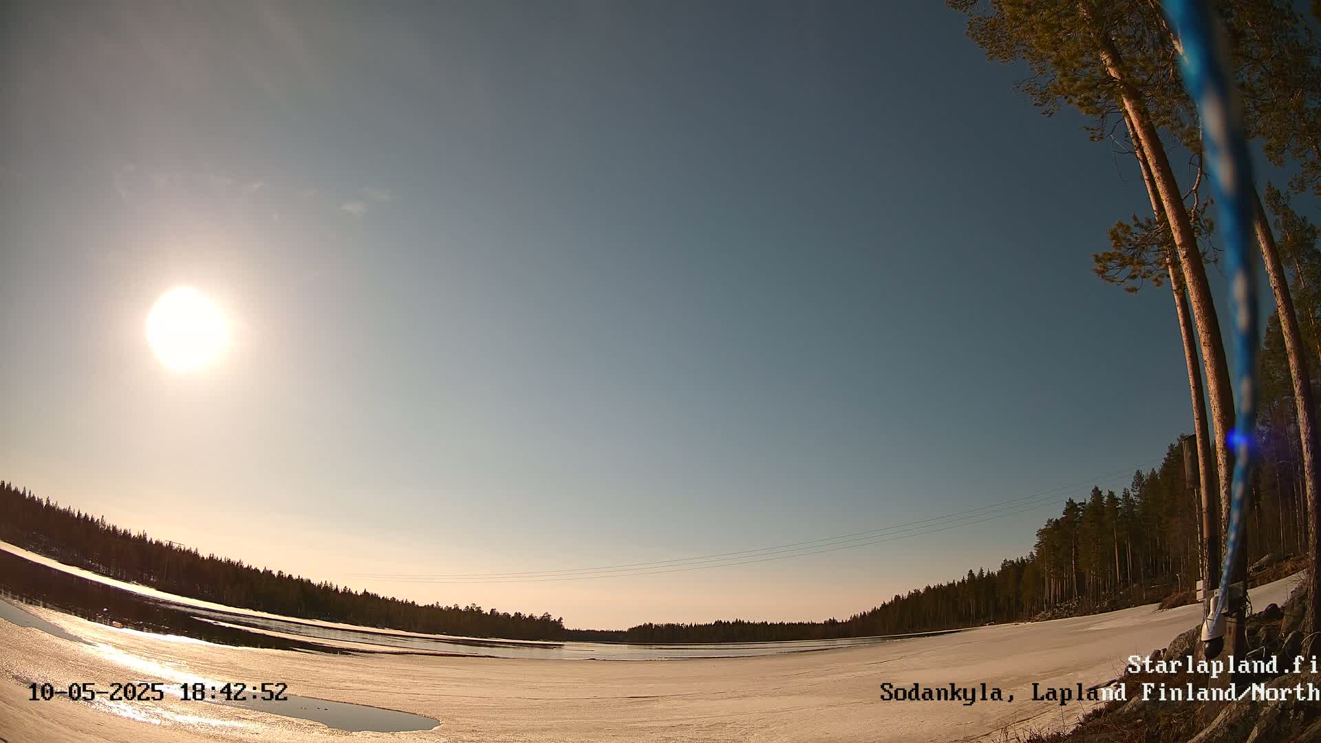 A mostly clear, sunny sky over a snow-covered landscape with a frozen body of water and a line of trees in the distance.