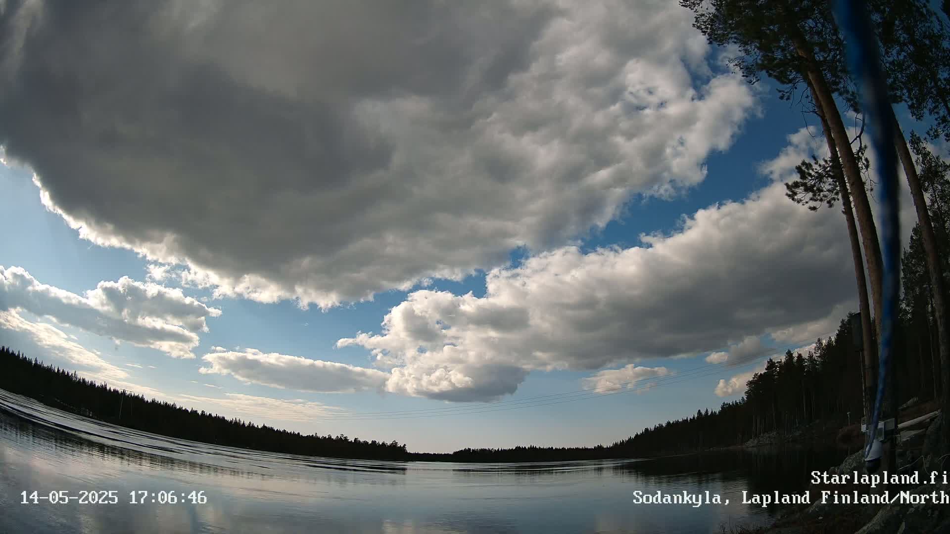 A partly cloudy sky over a calm lake with a dark forest in the background.