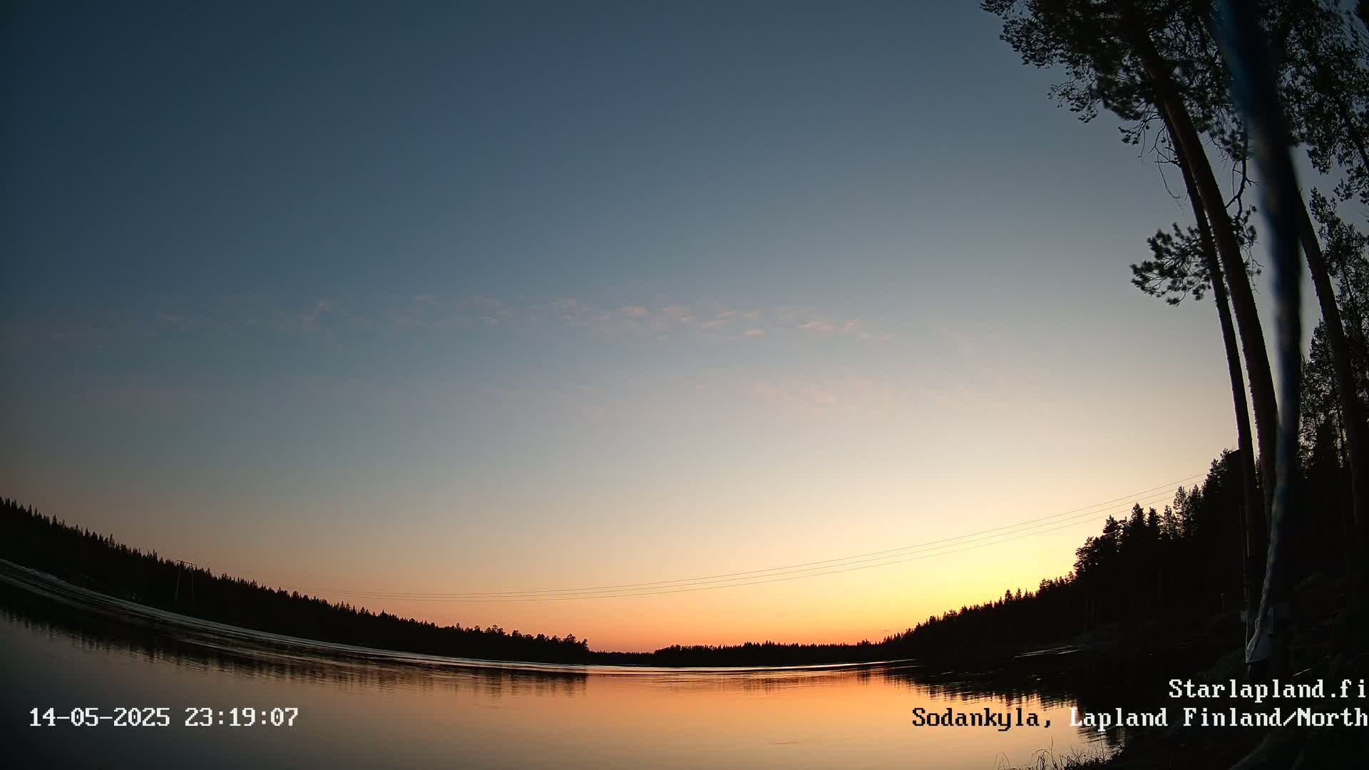 A calm lake reflects a sunset sky under a mostly clear twilight sky, with dark silhouetted trees lining the shore.