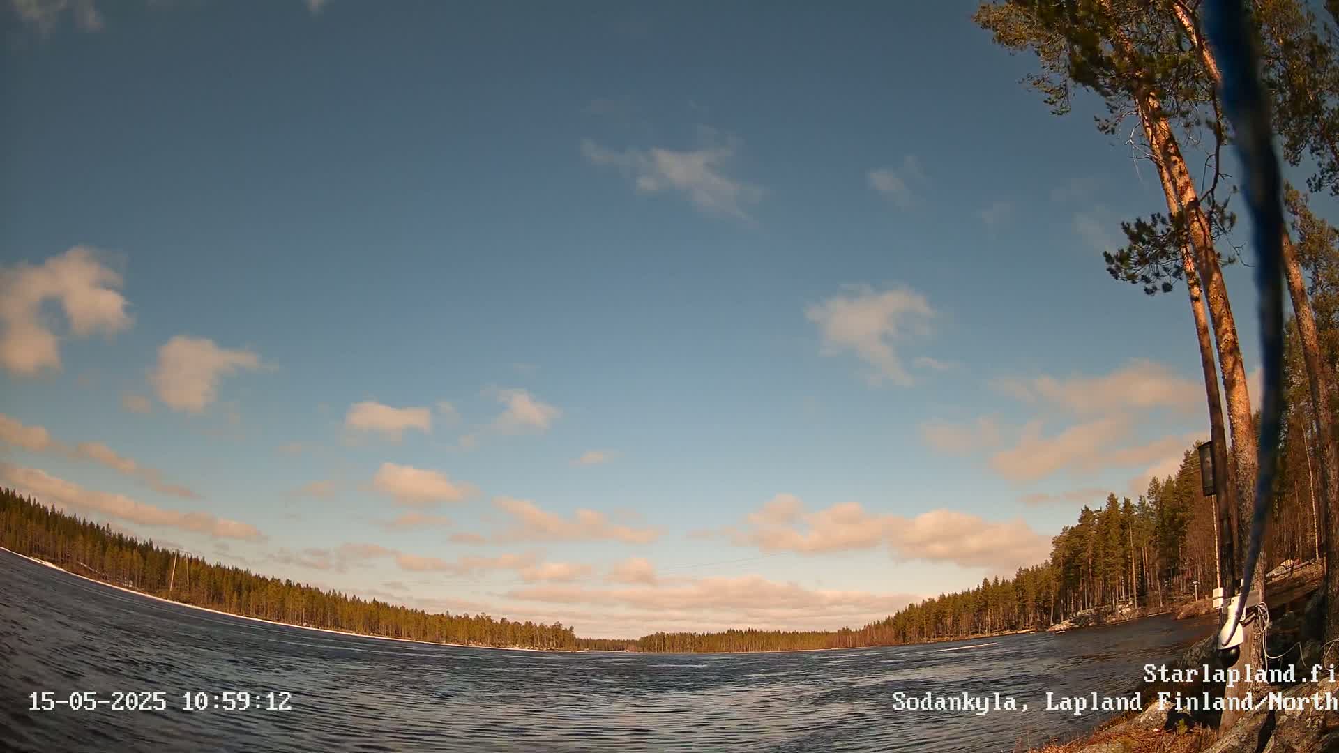 A mostly sunny day with scattered clouds over a calm lake bordered by a dark evergreen forest.