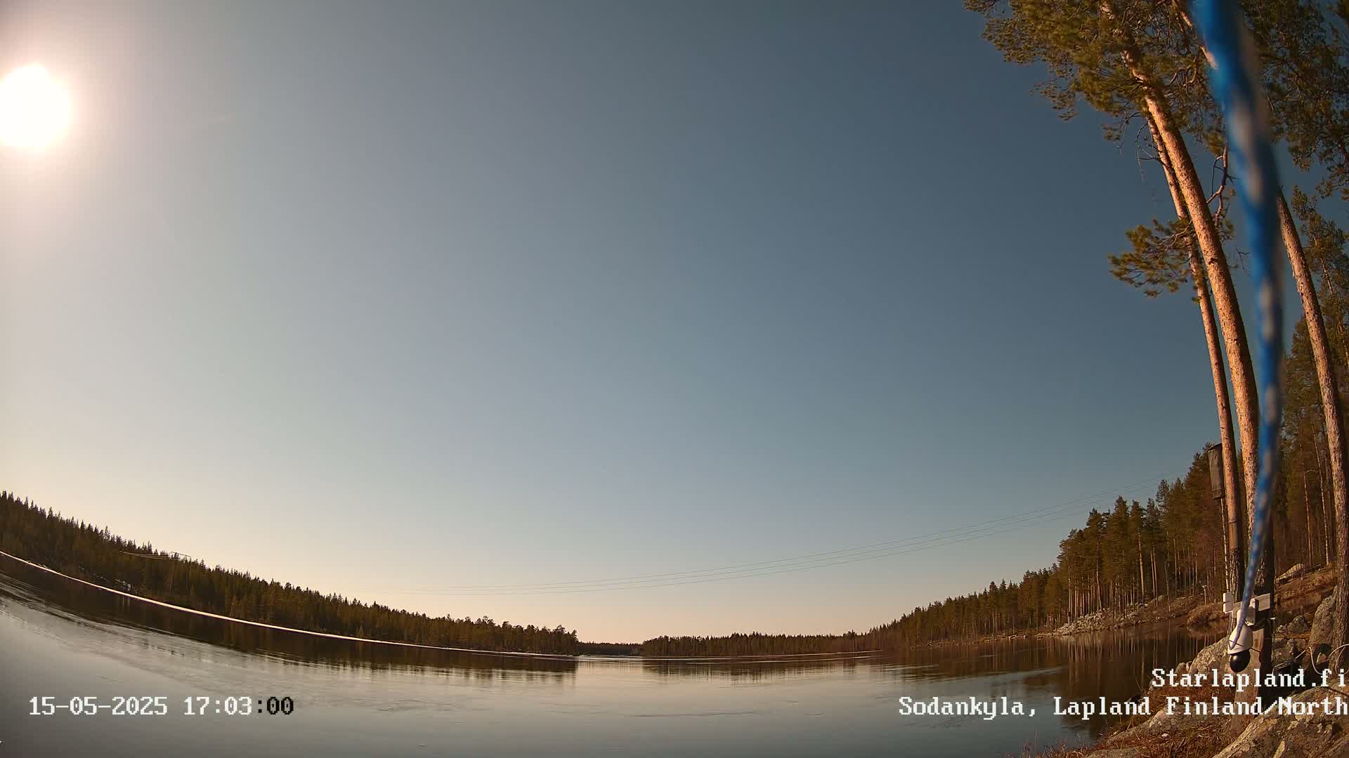A calm, sunlit river reflects a treeline under a clear, pale blue sky.