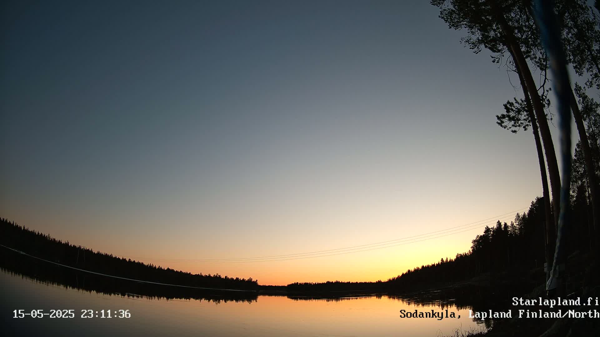 A calm lake reflects a sunset sky over a dark, silhouetted treeline.
