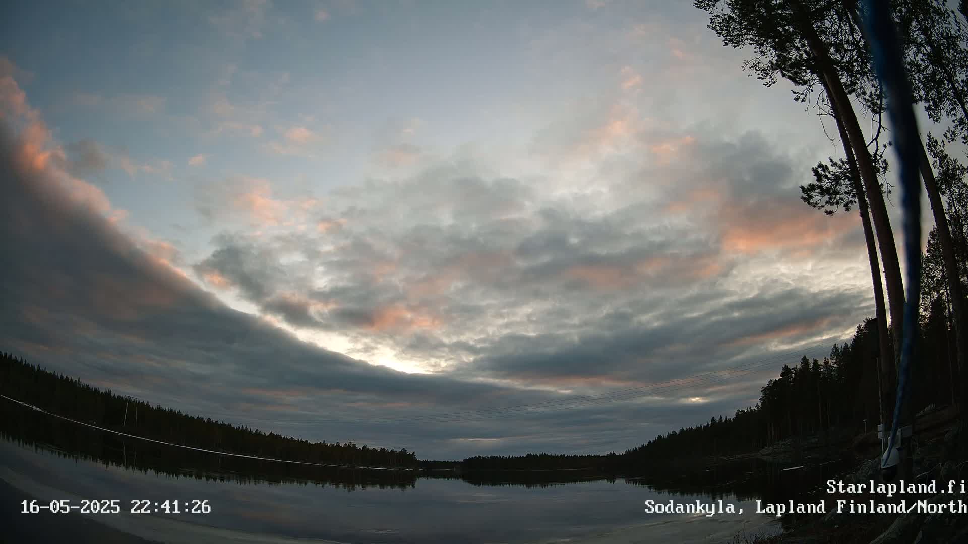 A calm lake reflects a twilight sky filled with mostly gray clouds, with streaks of pink and orange near the horizon.