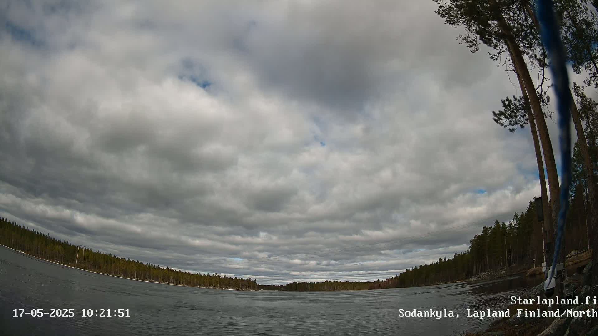 A wide, overcast sky over a calm river bordered by a dark green forest.