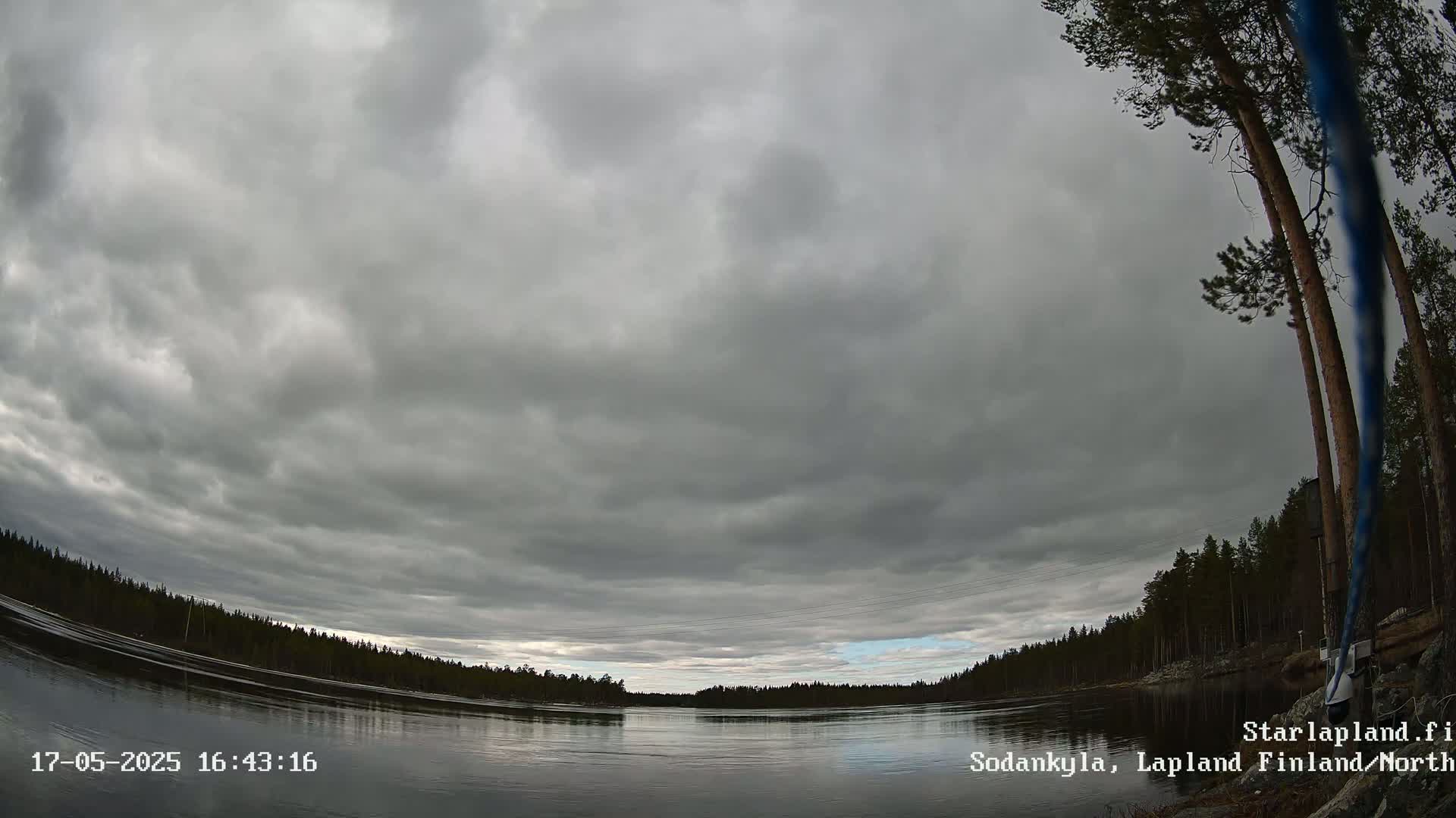 A wide, overcast sky hangs over a calm river surrounded by a dark evergreen forest.