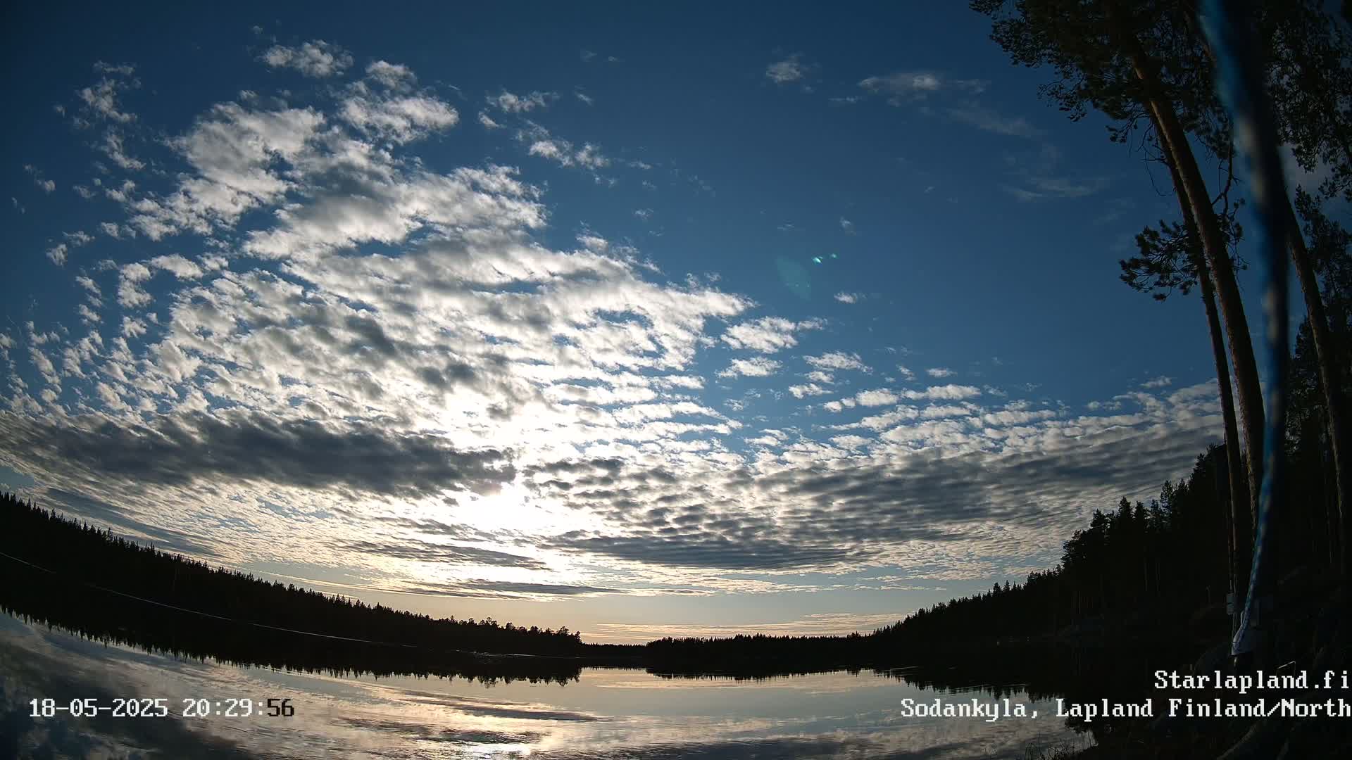 A calm lake reflects a sunset sky filled with numerous small, fluffy clouds.