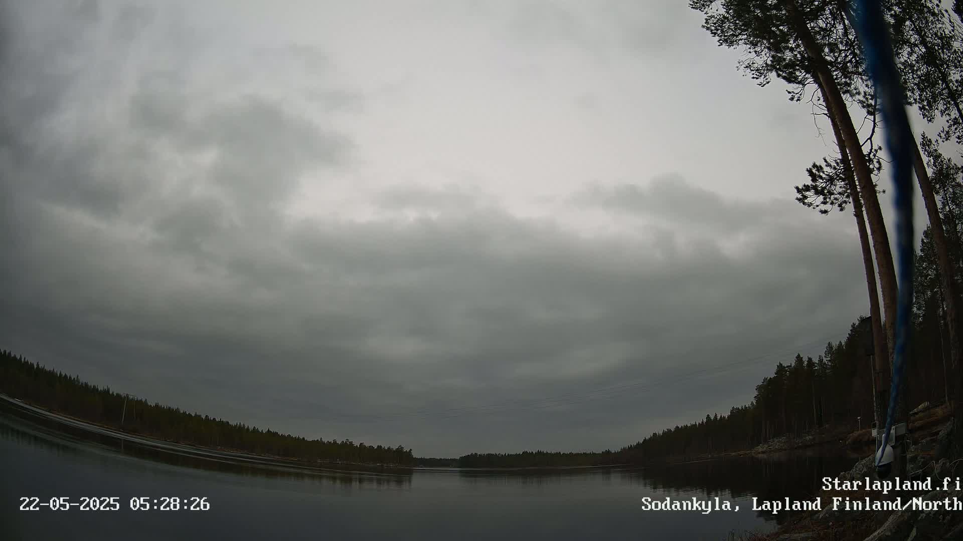 A calm body of water is surrounded by a dark, overcast sky and a treeline of evergreen trees.