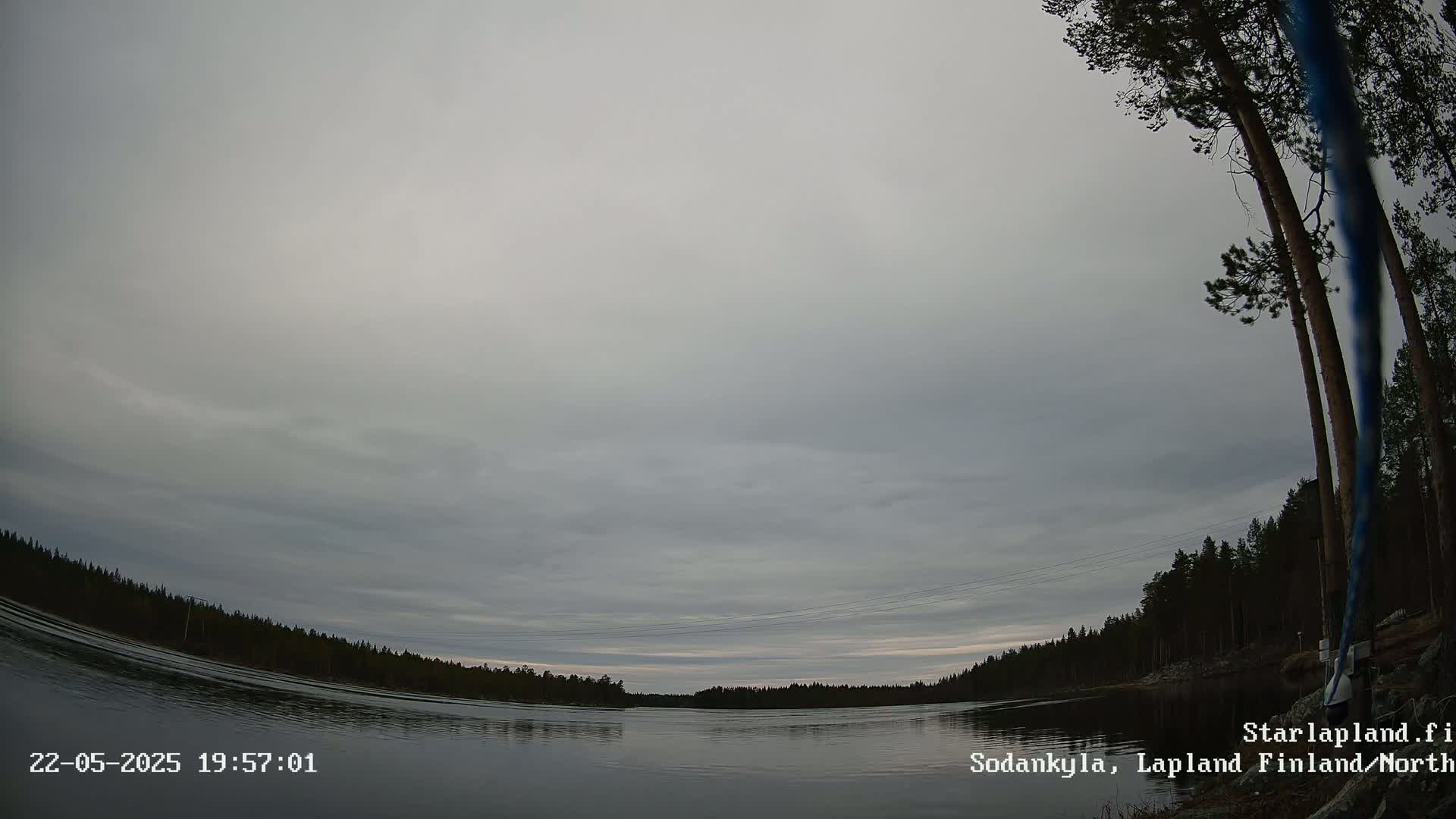 A calm body of water reflects a cloudy, overcast sky under which a dark line of trees is visible on the far shore.