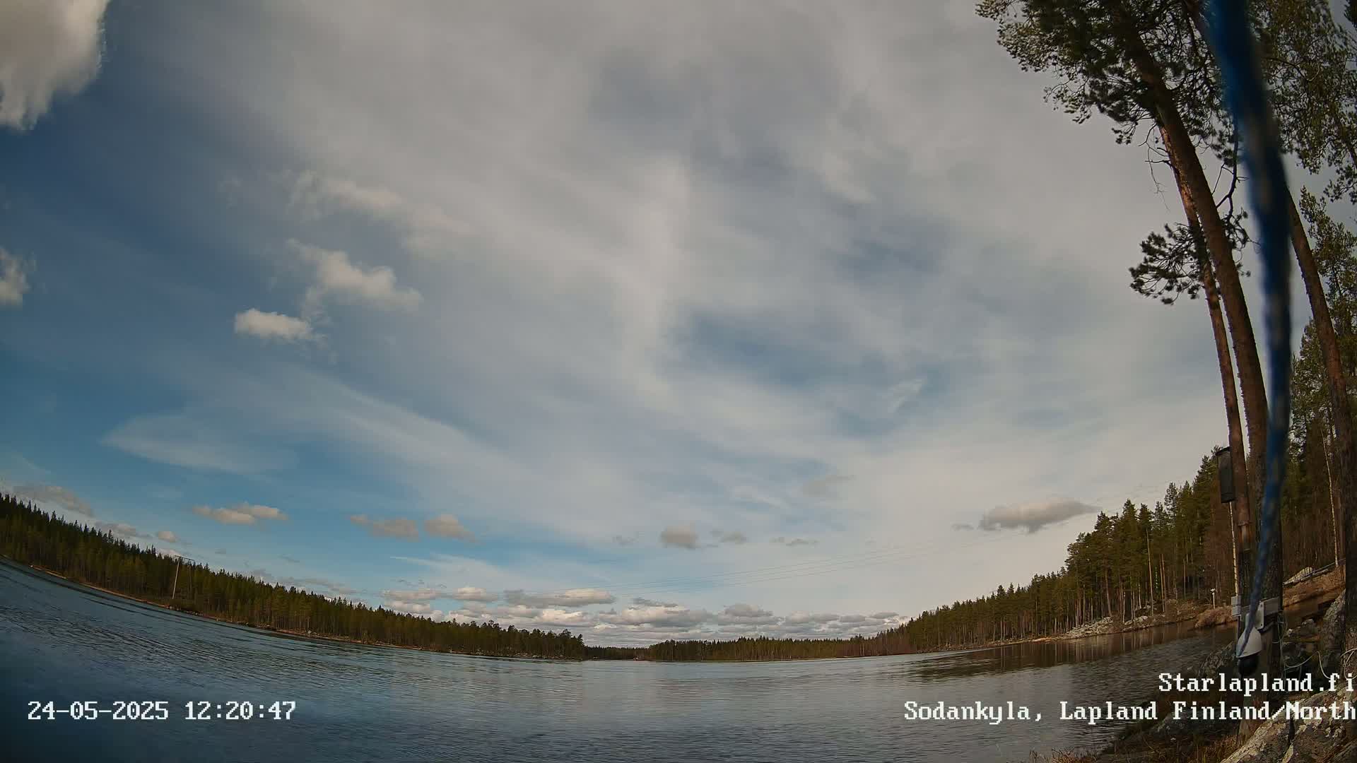 A mostly cloudy sky over a calm lake surrounded by a dark green forest.