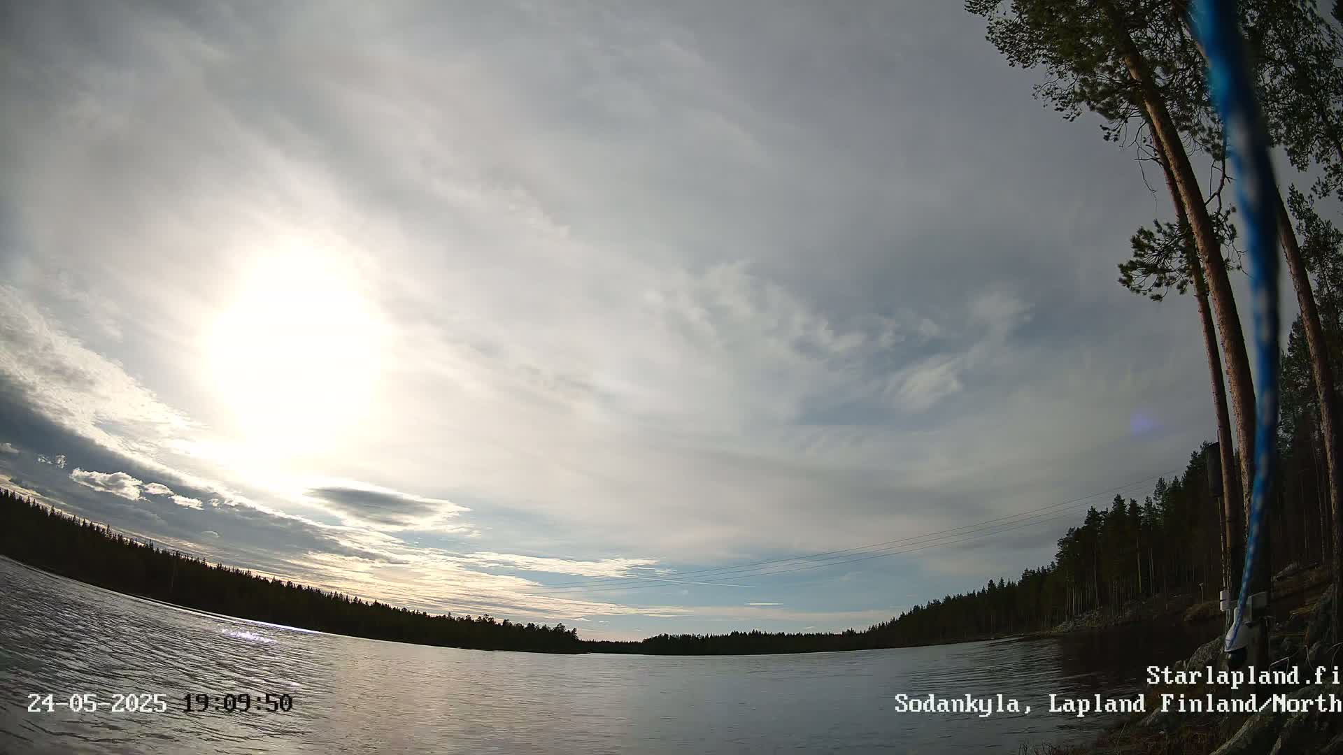A partly cloudy sky over a calm lake surrounded by a dark evergreen forest.