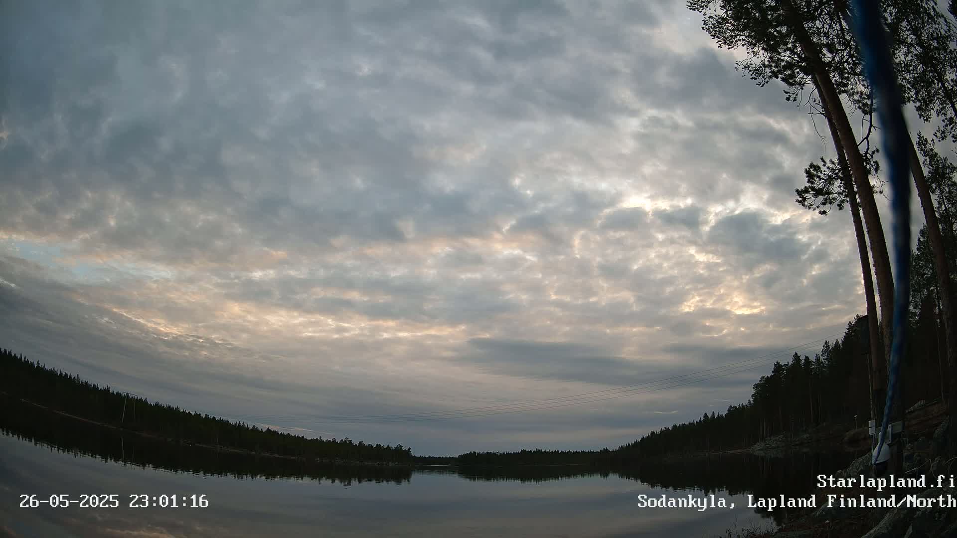 A calm lake reflects a mostly cloudy sky with hints of sunset, surrounded by a dark silhouetted forest under a mostly cloudy sky.
