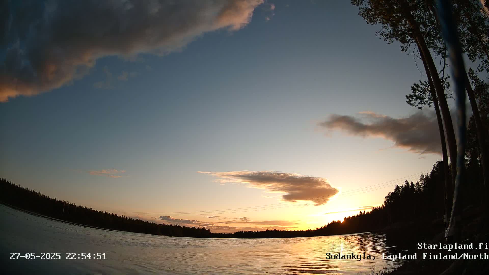 A calm lake at sunset under a partly cloudy sky, with silhouetted trees lining the shore.