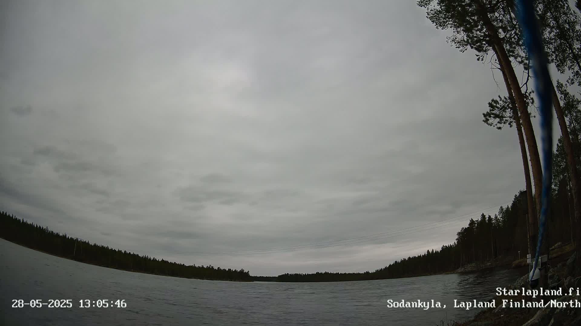 A wide, overcast sky hangs over a calm lake bordered by a dark, coniferous forest.