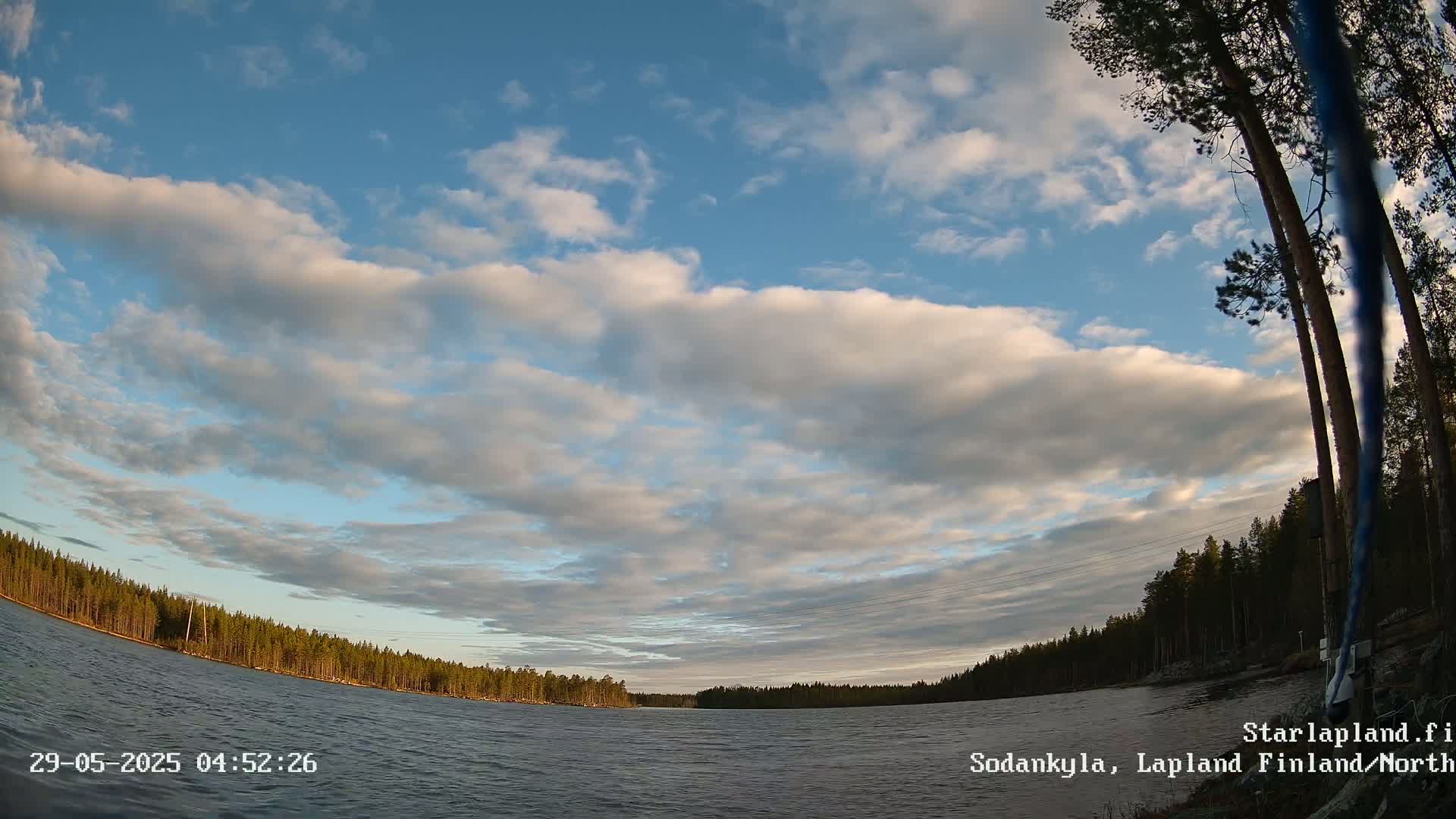 A partly cloudy sky over a calm lake surrounded by a dark green forest.