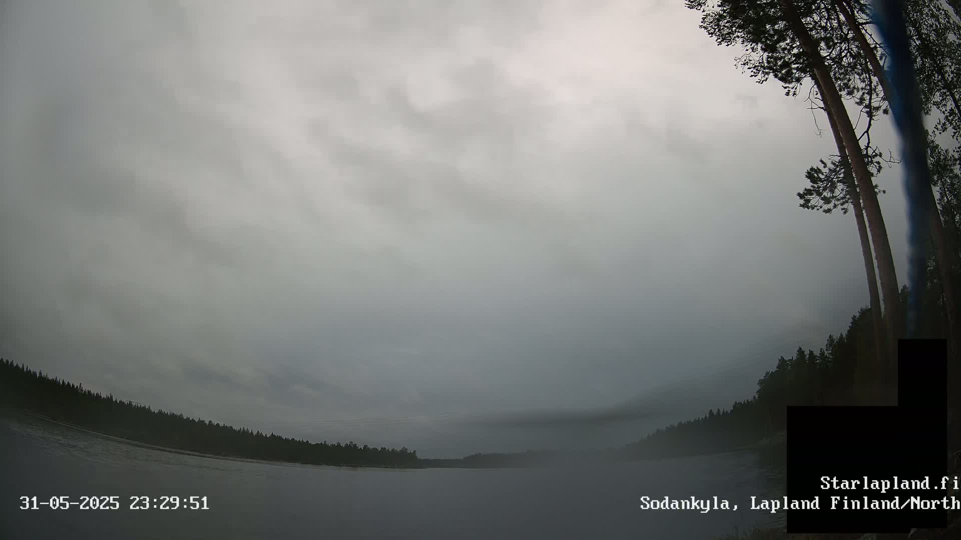 A wide shot of a calm body of water under an overcast sky, with a dark forest visible on the opposite shore.