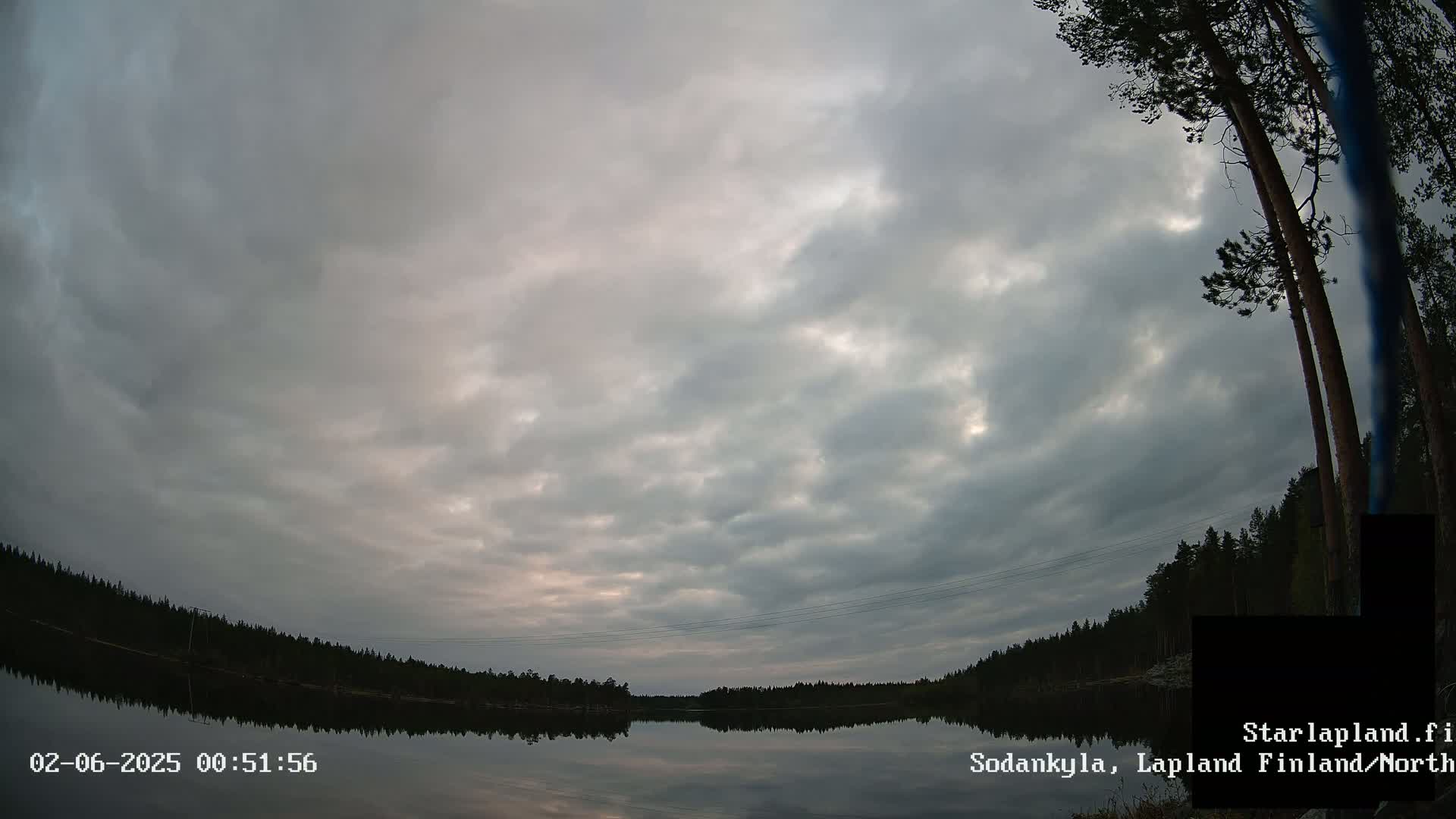 A calm lake reflects a cloudy sky at dawn, with a line of trees along the far shore.