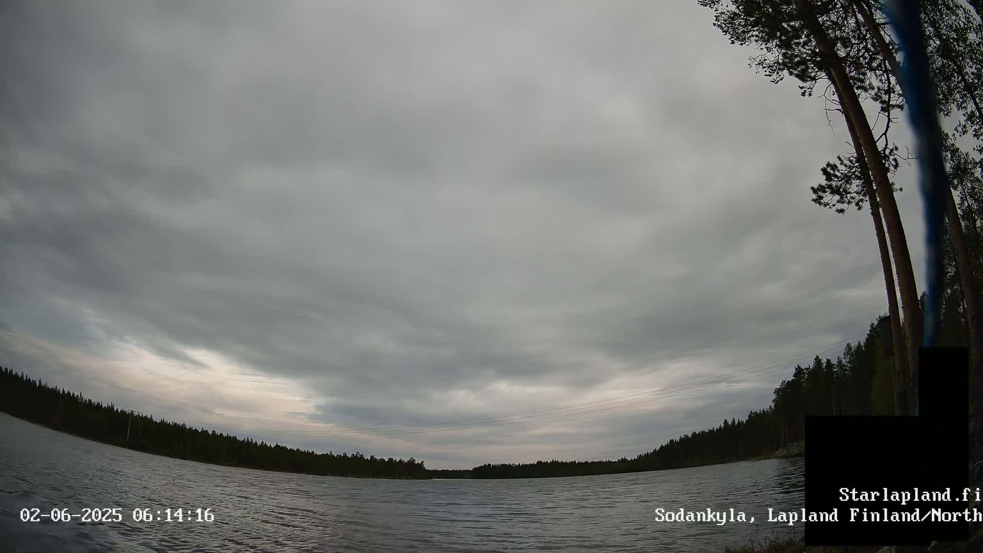 A mostly cloudy sky hangs over a calm lake bordered by a dark line of trees.