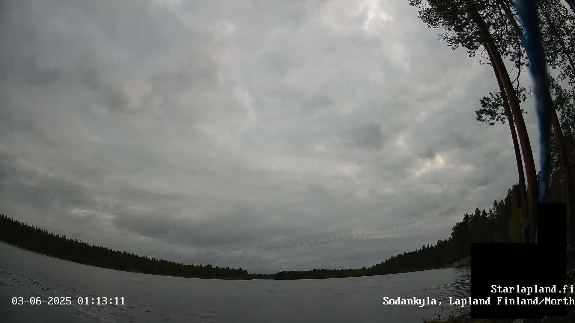 A calm body of water is shown under an overcast sky, with a treeline visible on the far shore.