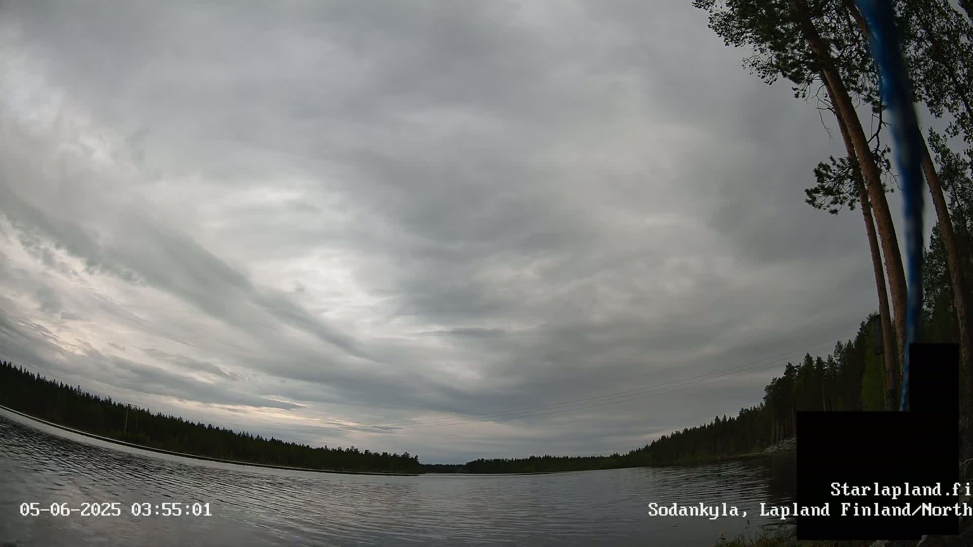 A calm lake is surrounded by a dark, overcast sky and a treeline.