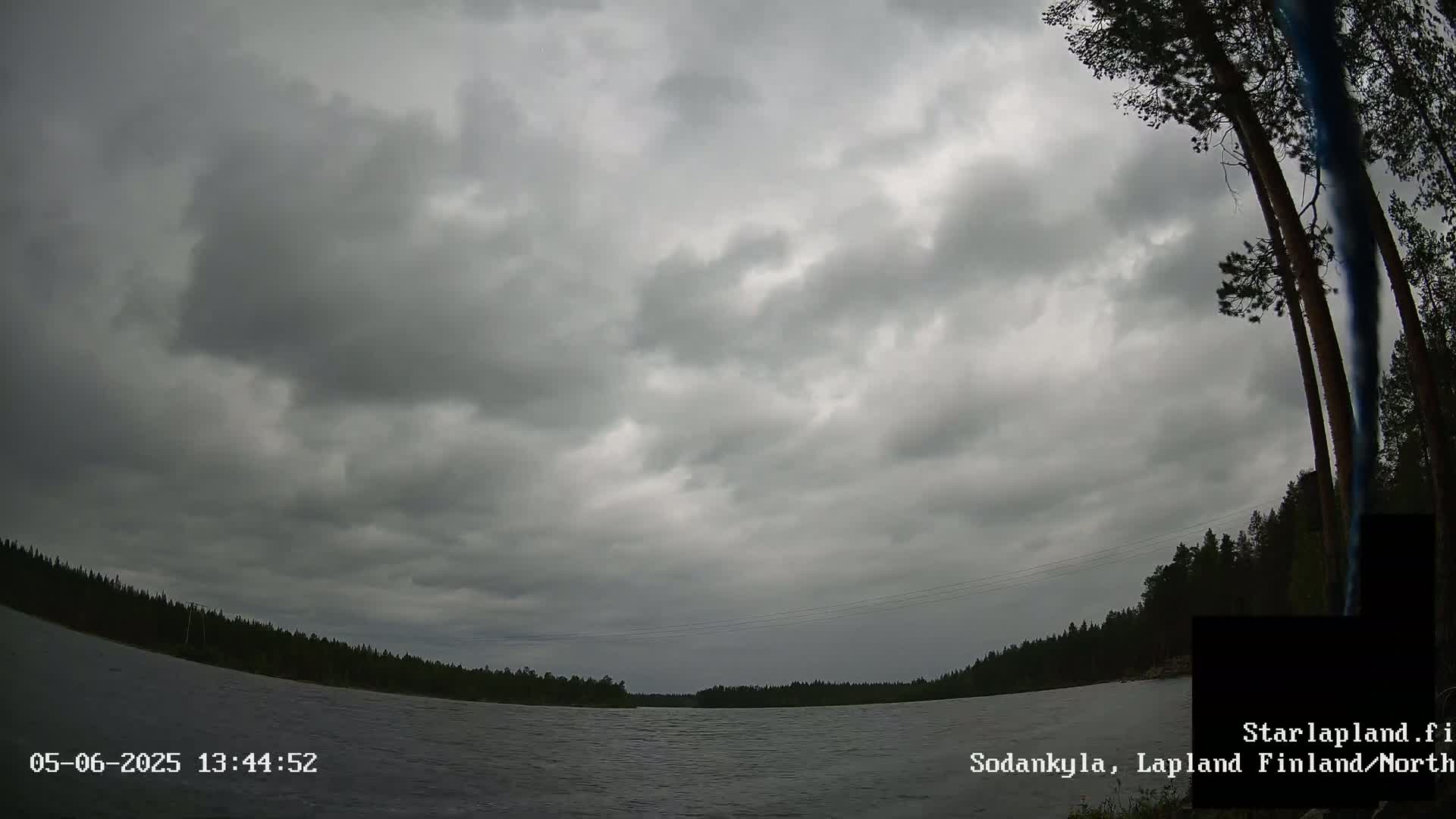 A mostly cloudy sky over a calm lake, bordered by dark green trees under an overcast sky.