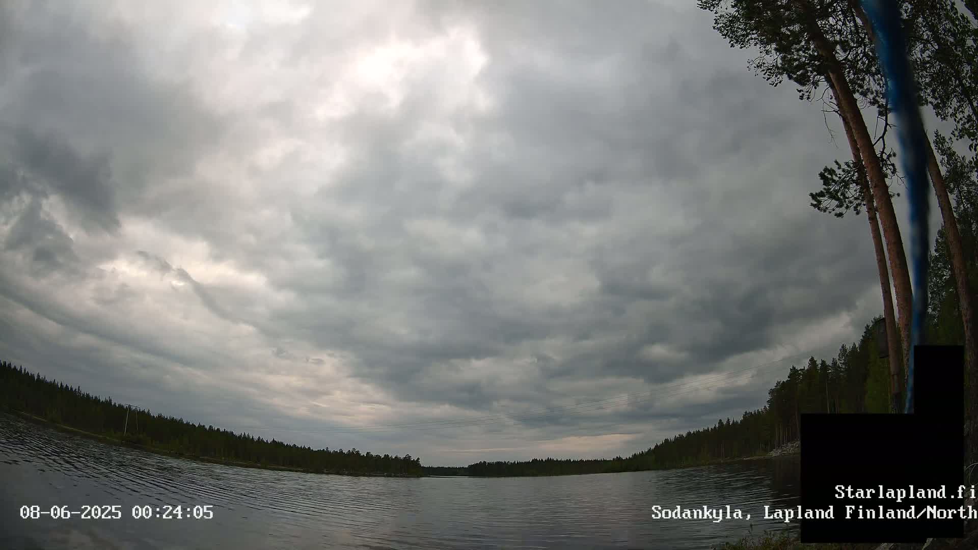 A calm lake is surrounded by a dark forest under a heavily overcast sky.