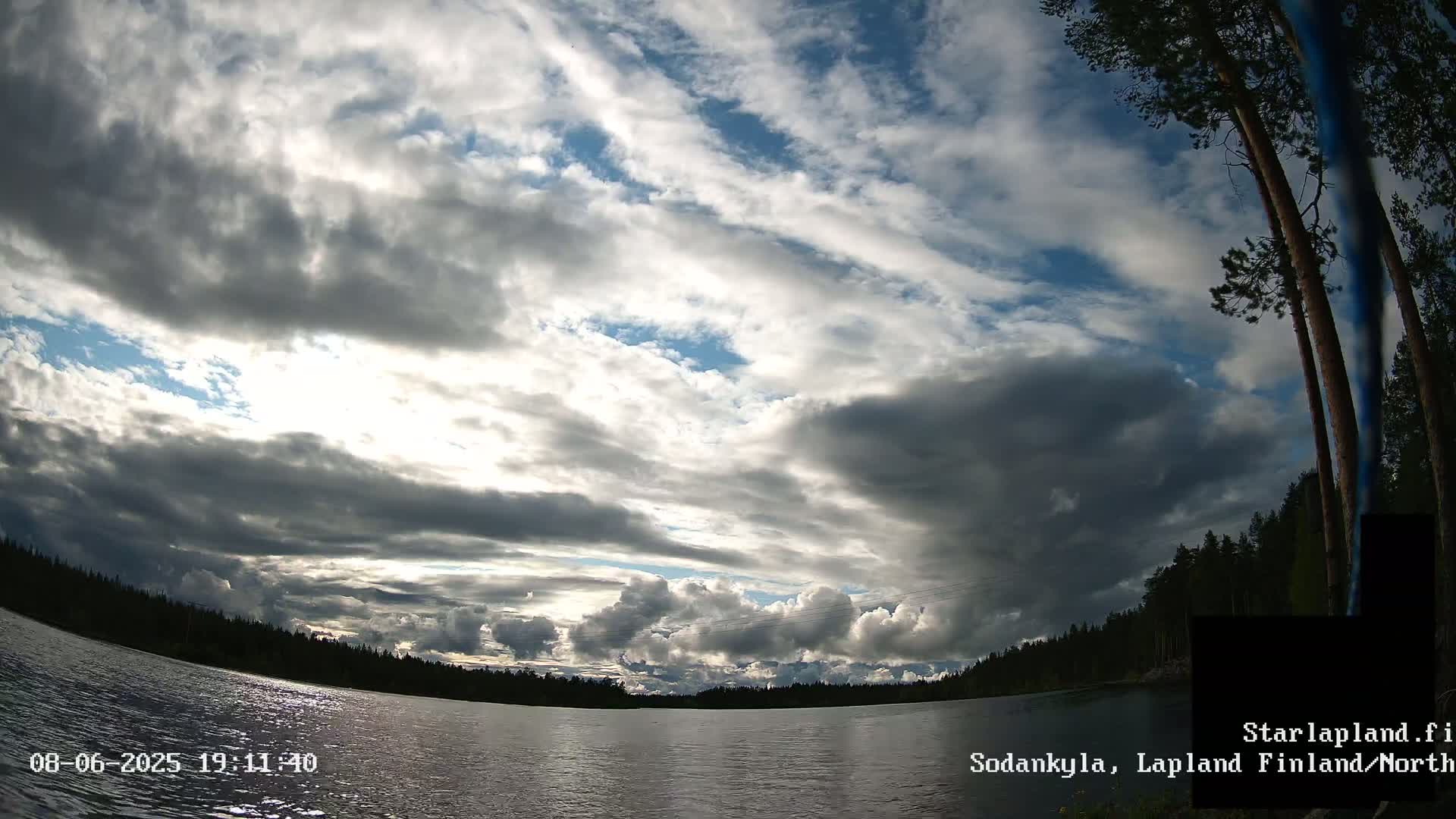 A partly cloudy sky over a calm lake surrounded by dark green trees.