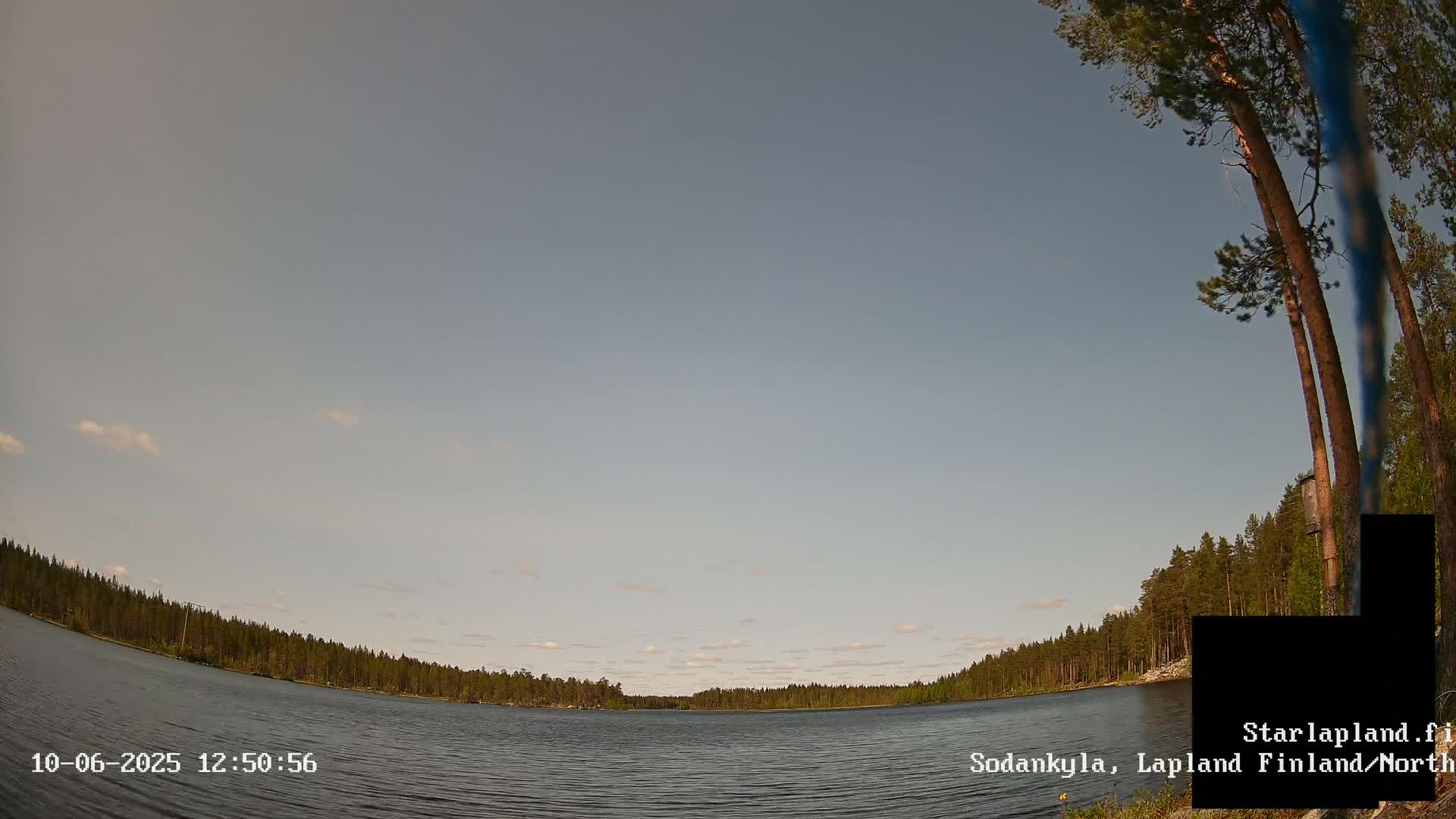 A calm lake is surrounded by a dense forest under a mostly clear, light-grey sky.