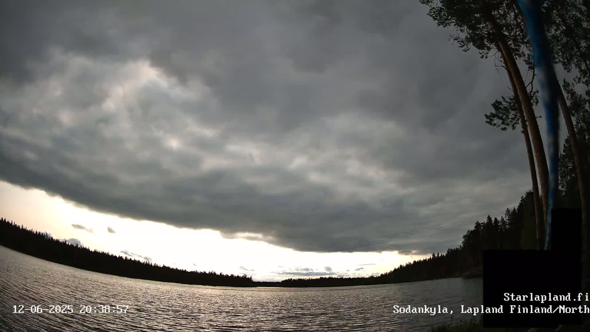 A dark, overcast sky hangs over a calm lake surrounded by a dark forest.