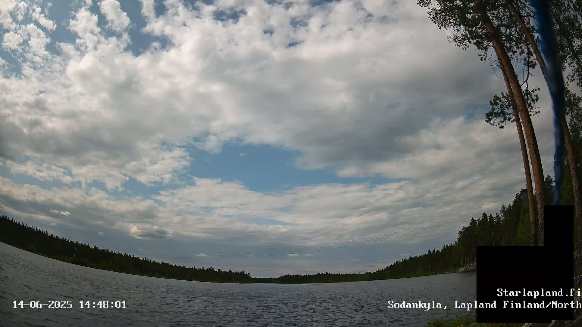 A partly cloudy sky overlooks a calm lake surrounded by a dark green forest.
