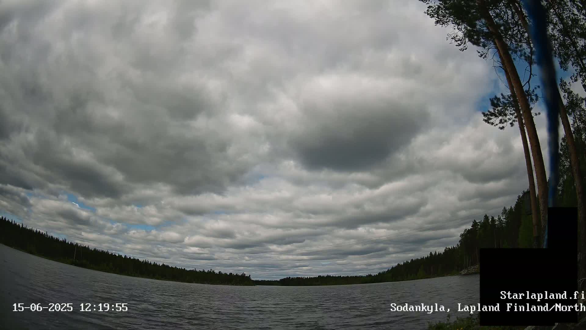 A mostly cloudy sky over a calm lake surrounded by a dark green forest.
