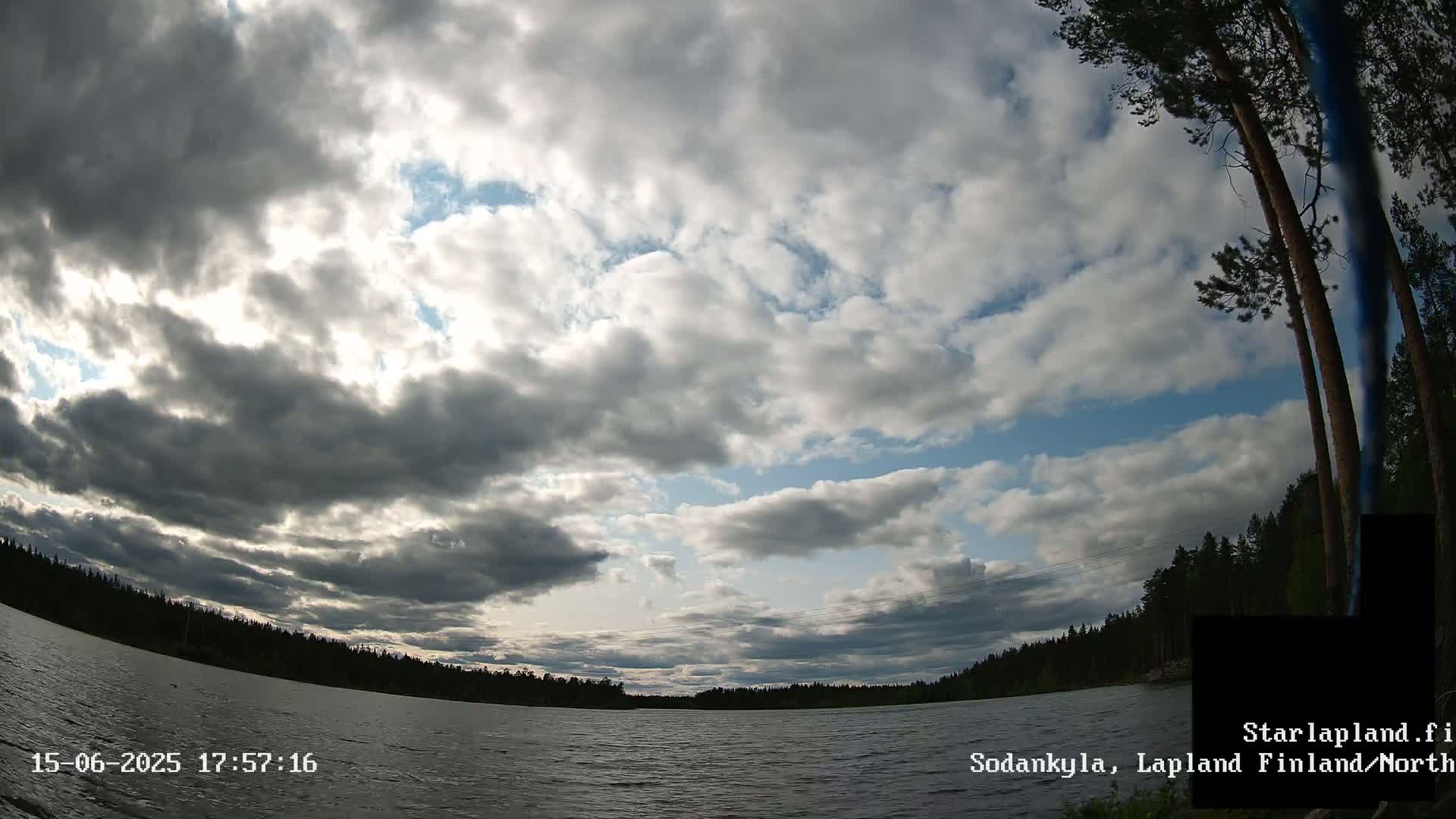A mostly cloudy sky over a calm lake surrounded by a dark green forest.