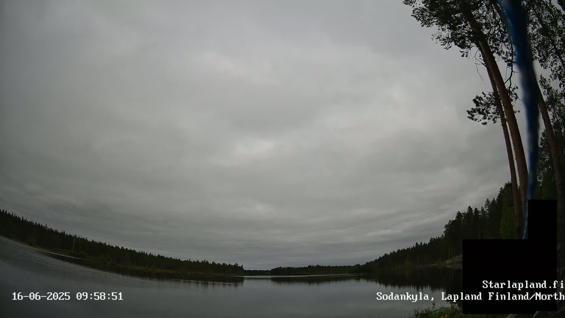 A mostly cloudy sky over a calm lake surrounded by a dark green forest.