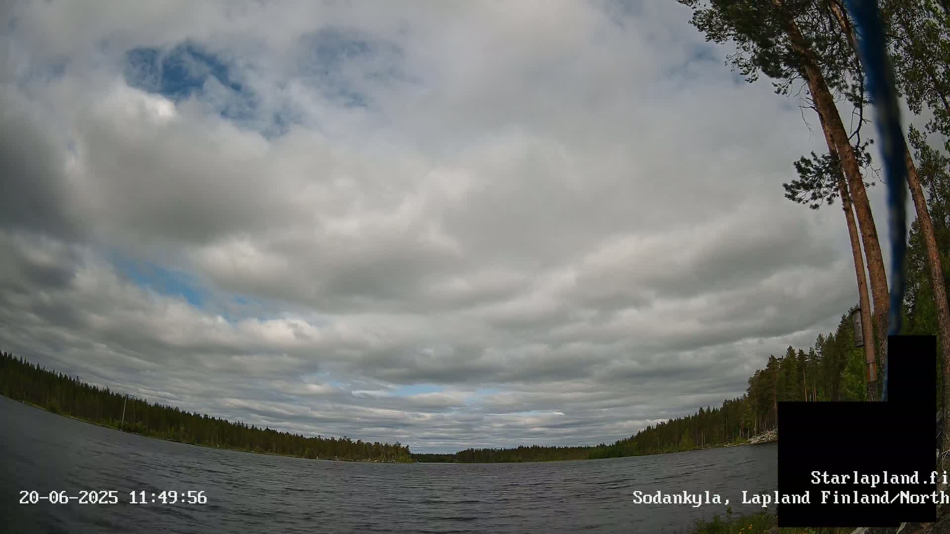 A mostly cloudy sky over a calm lake surrounded by a dark green forest.