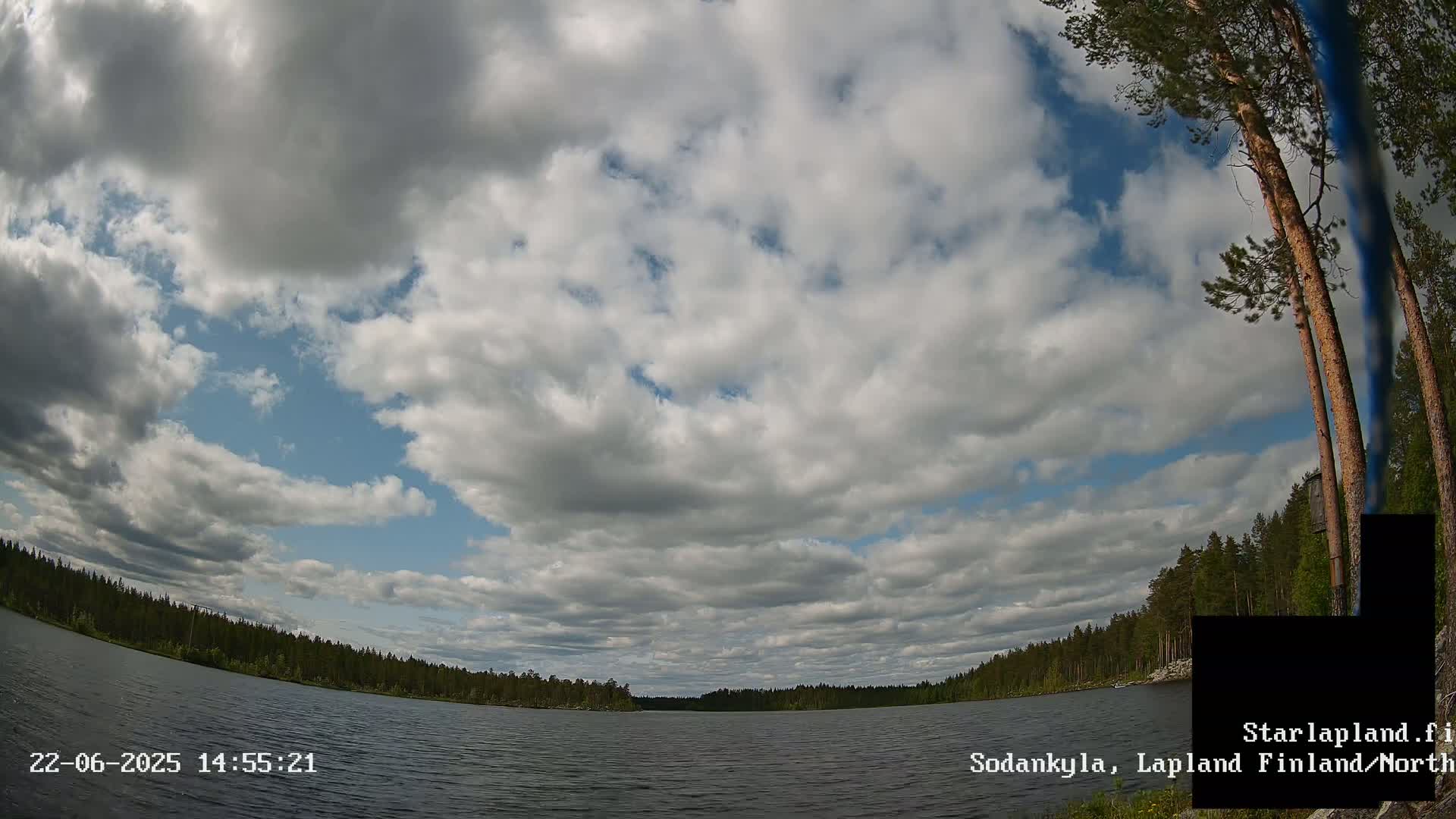 A mostly cloudy sky over a calm lake surrounded by a dark green forest.