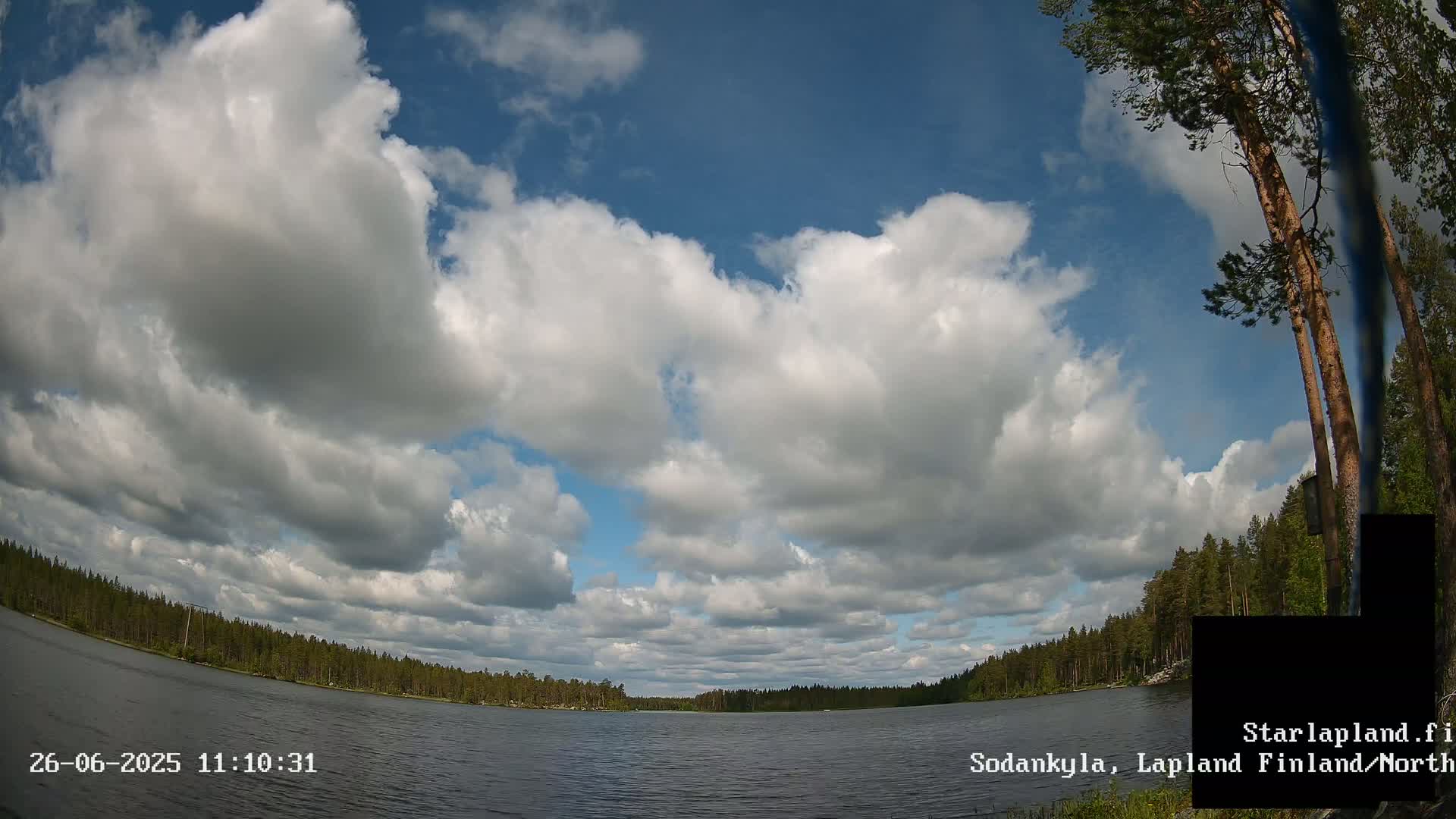 A partly cloudy sky over a calm lake surrounded by a coniferous forest.