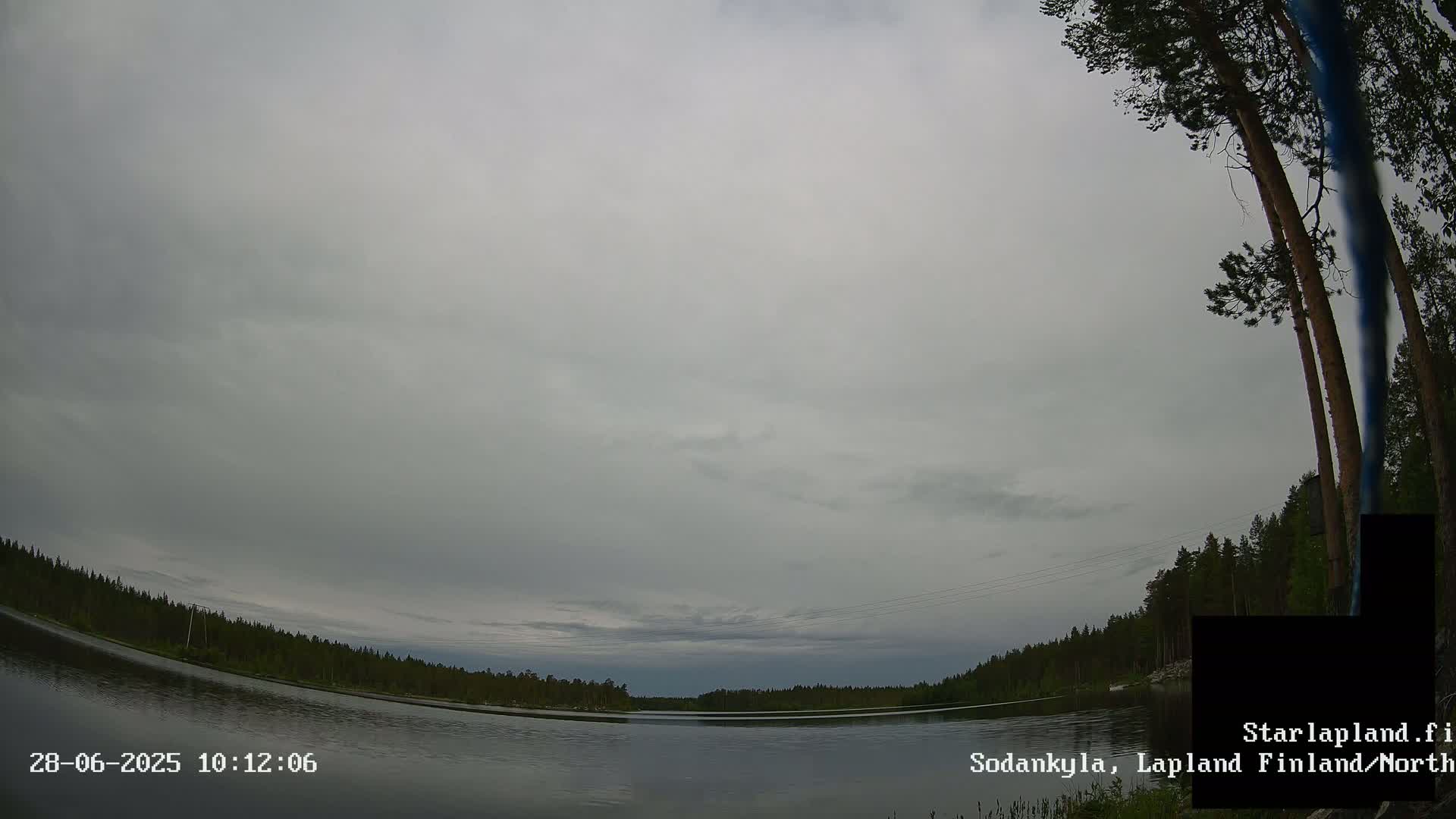 A calm lake is surrounded by a dark green forest under an overcast sky.