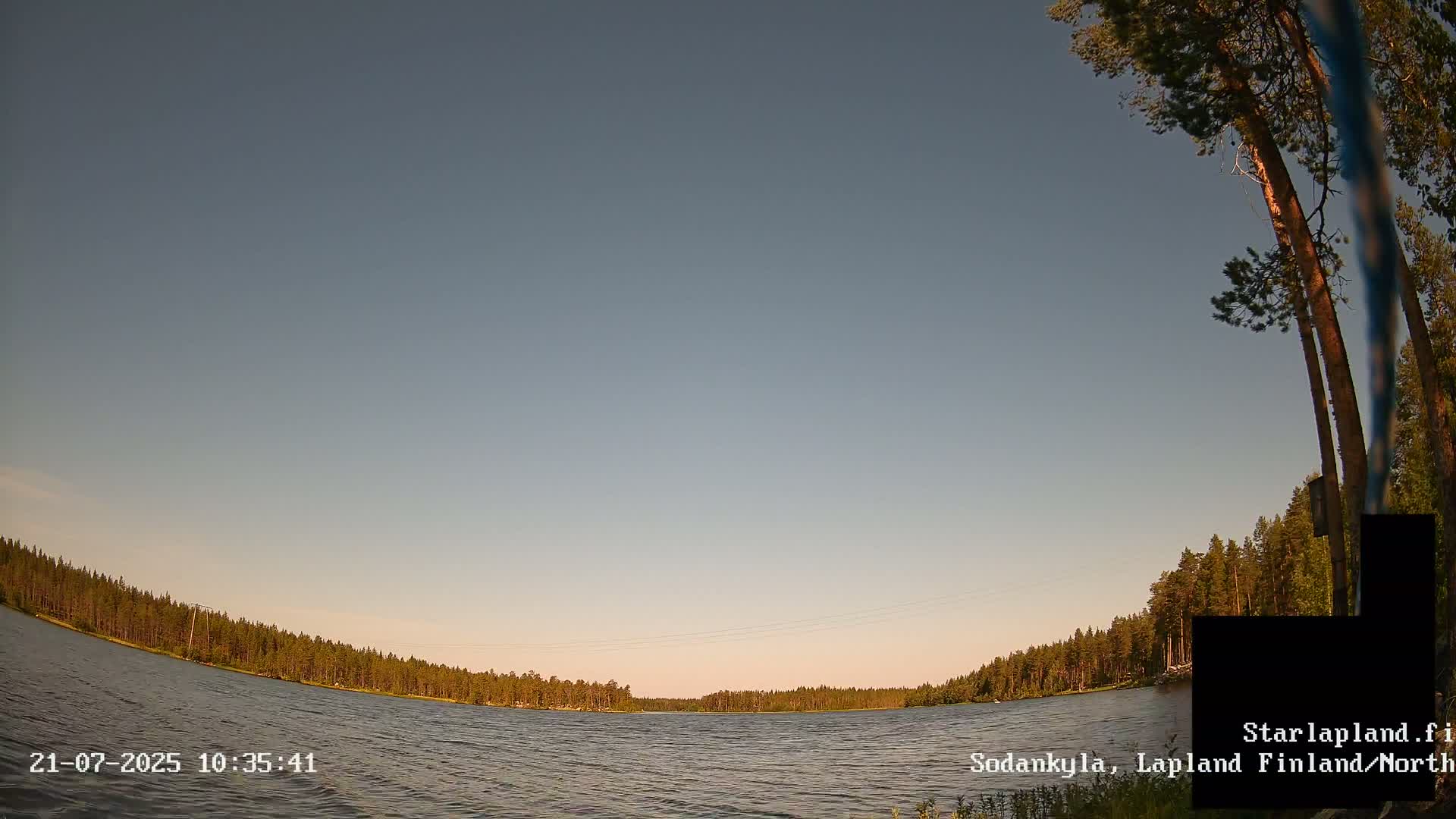 A calm lake is surrounded by a dark green forest under a clear, light blue sky.