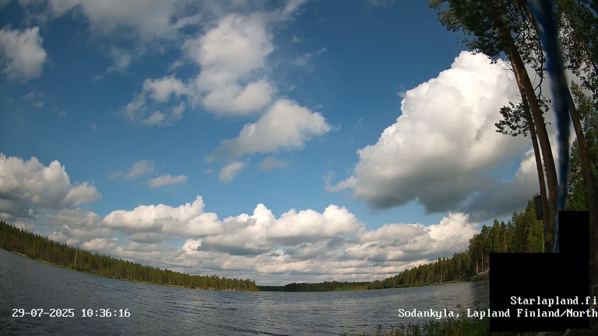 A calm lake is surrounded by a dense forest under a partly cloudy sky.