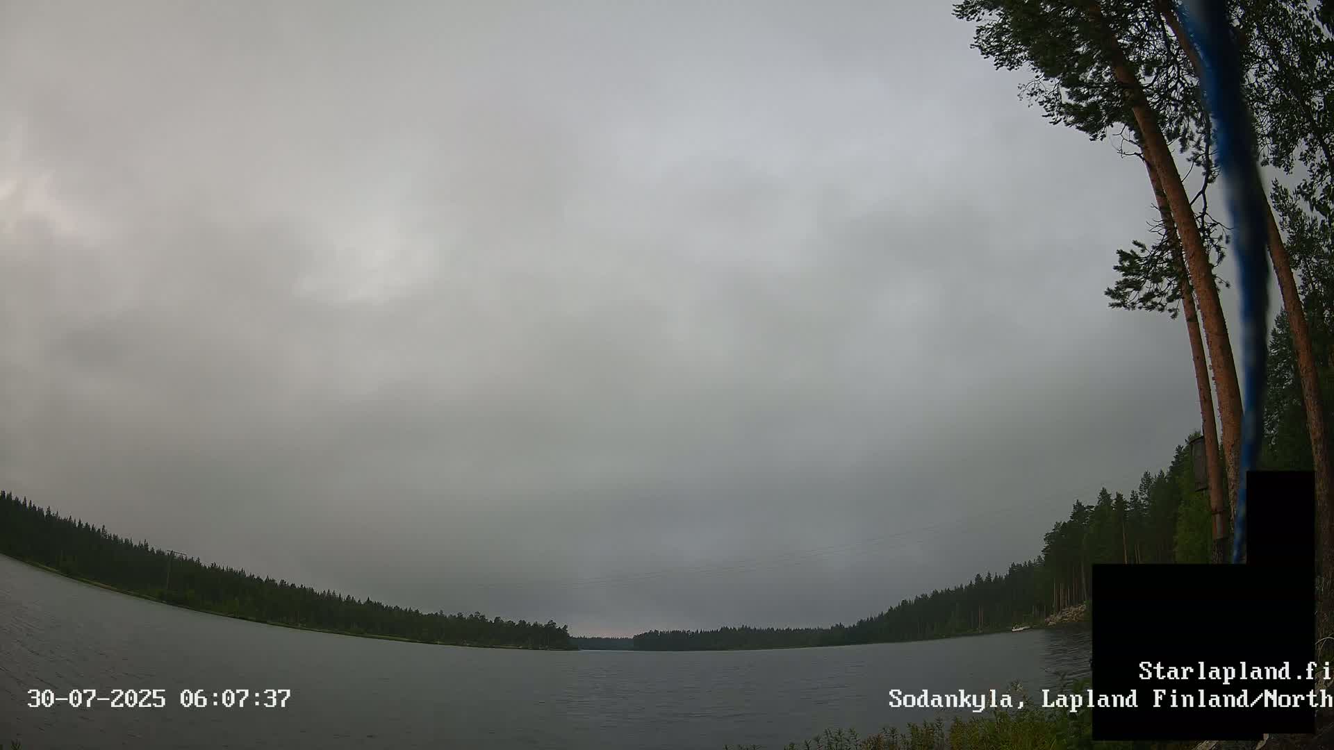 A calm lake is surrounded by a dense forest under a partly cloudy sky.