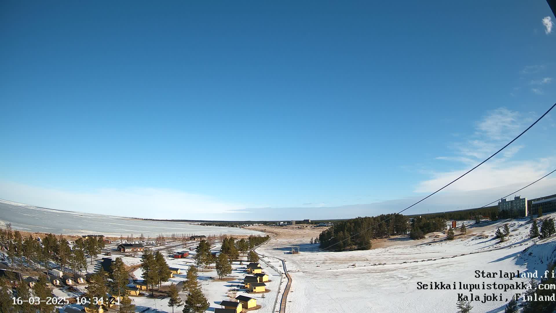 A snow-covered landscape with small yellow buildings near a frozen lake under a clear blue sky.