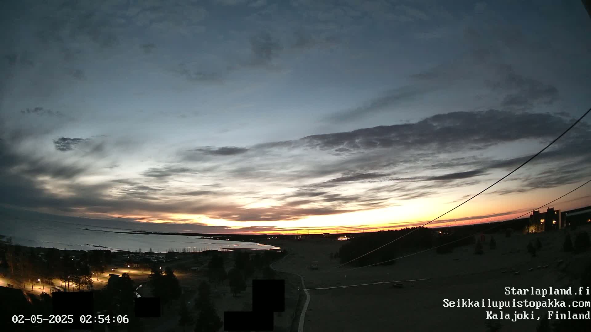 A partly cloudy sunrise over a dark, mostly flat landscape with a body of water in the distance.