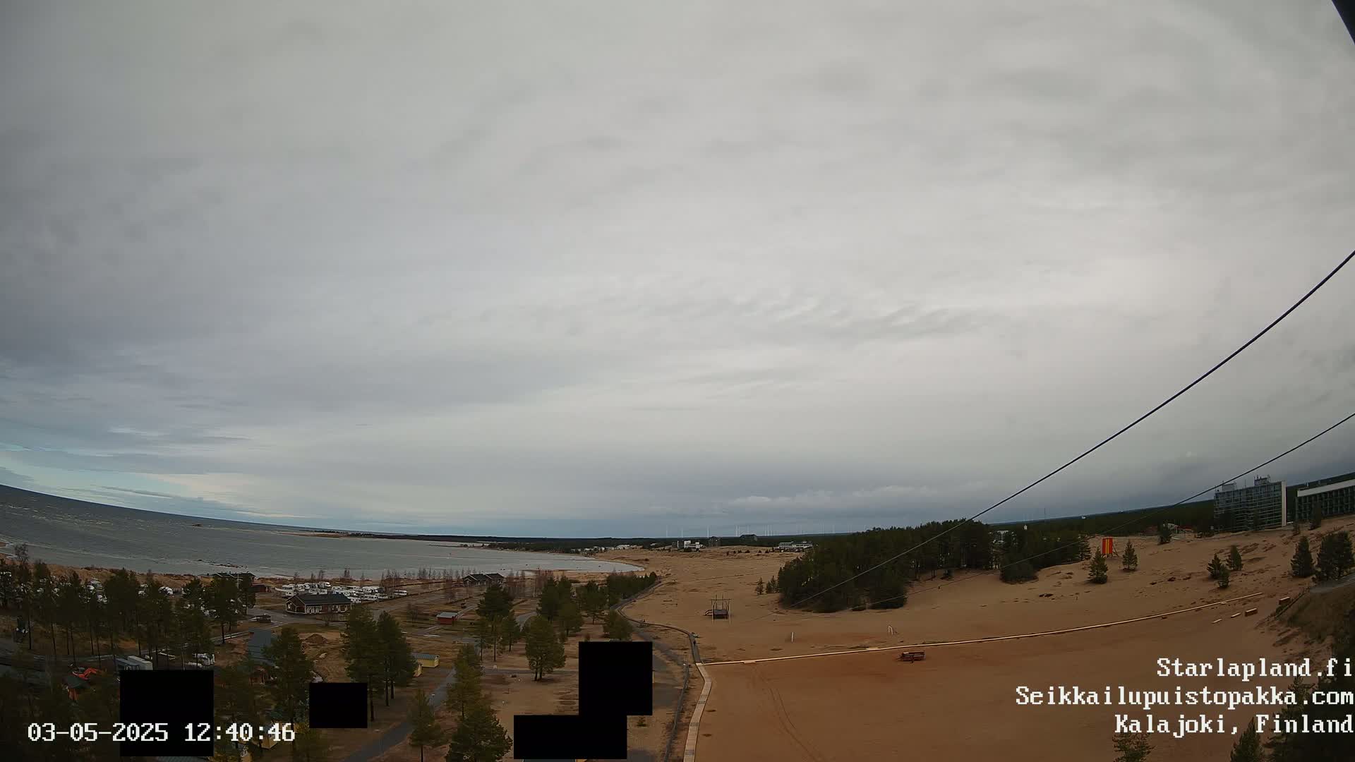A high-angle view shows a sandy area with sparse vegetation near a body of water under an overcast sky.